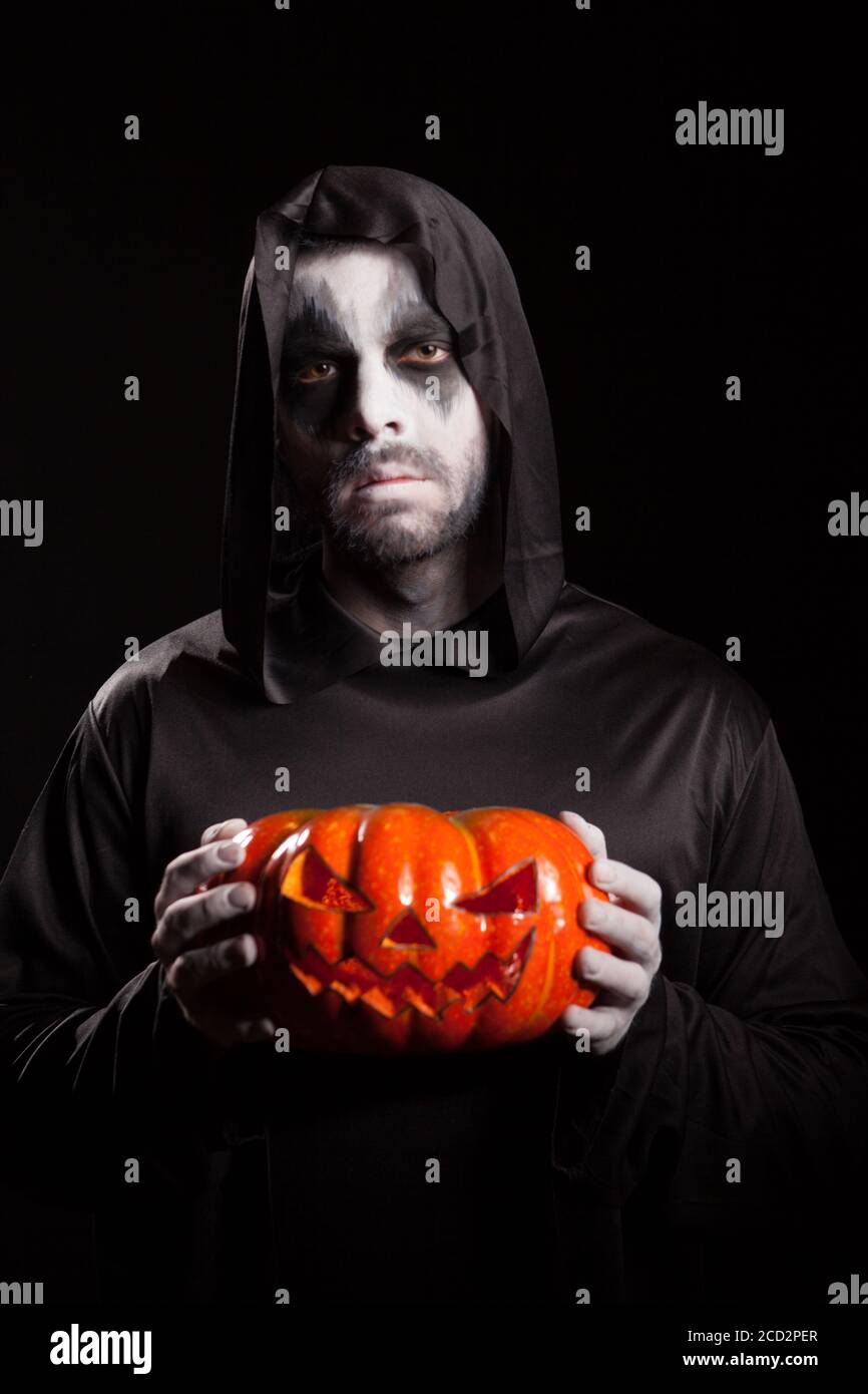 Gruseliger Grusel hält einen Kürbis über schwarzem Hintergrund, Halloween-Outfit. Stockfoto