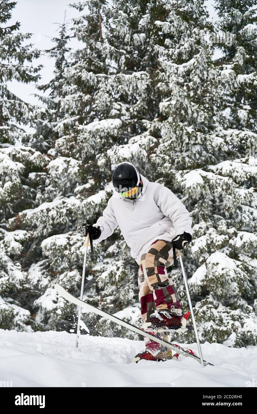 Skifahrer macht Tricks in den Bergen in der Wintersaison. Mann Freerider macht Sprung beim Rutschen nach schneebedeckten Pisten mit schönen schneebedeckten Fichtenwald im Hintergrund. Seitenansicht. Stockfoto