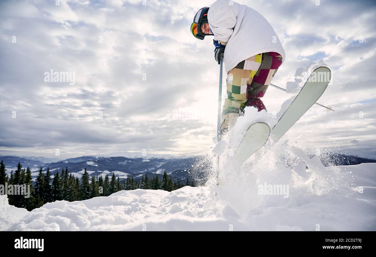 Nahaufnahme, Low-Angle-Ansicht Momentaufnahme der Beine des Skifahrers in bunten Skihosen machen einen Sprung auf weiße verschneite Oberfläche gegen schönen bewölkten Himmel. Speicherplatz kopieren. Konzept der Wintersport-Aktivitäten. Stockfoto