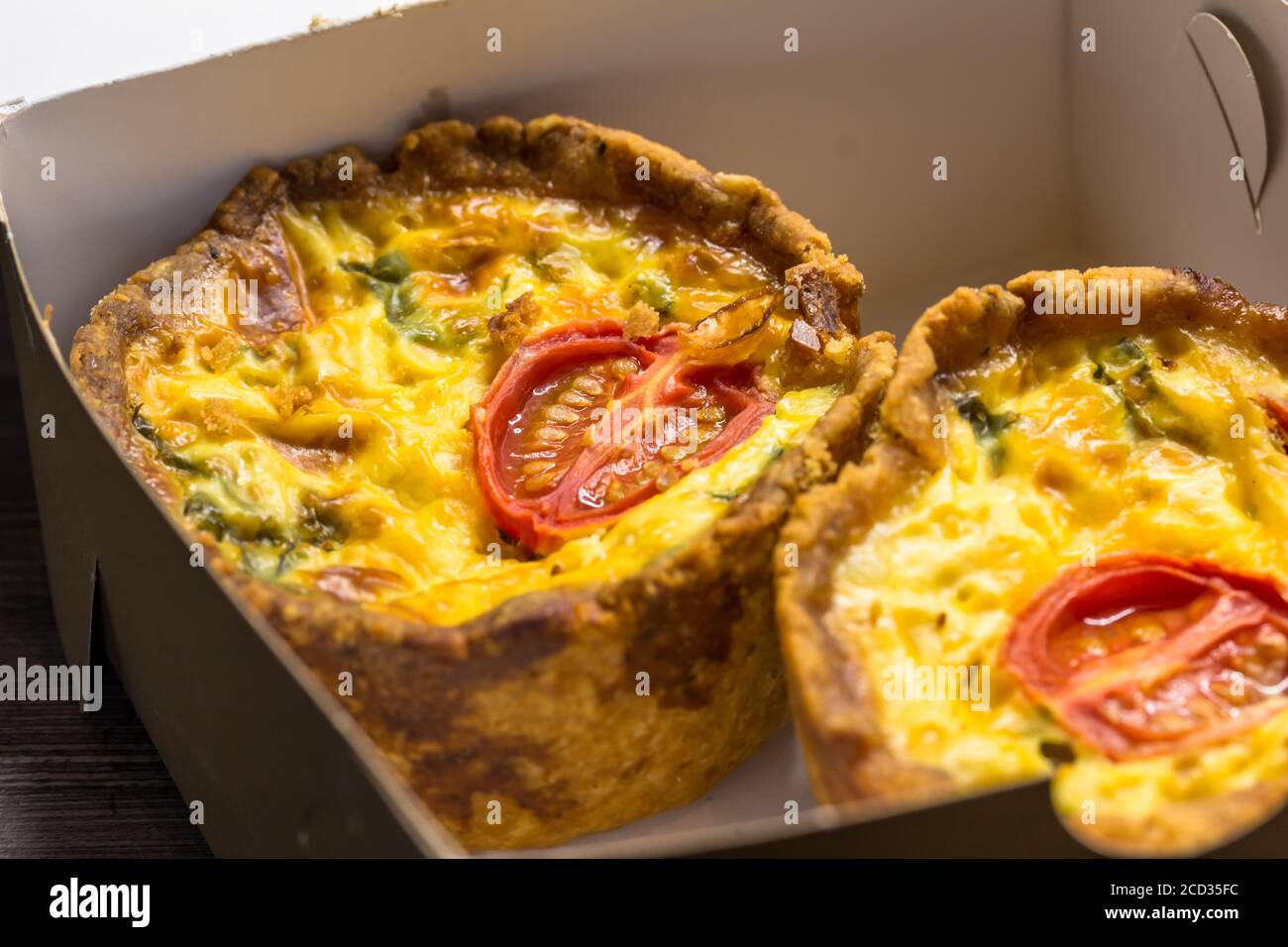 Zwei kleine Mini-Tomatentartlets in der Take-away-Box in Nahaufnahme - Bohnenkraut Mini Quiche Hintergrund mit selektivem Fokus Stockfoto