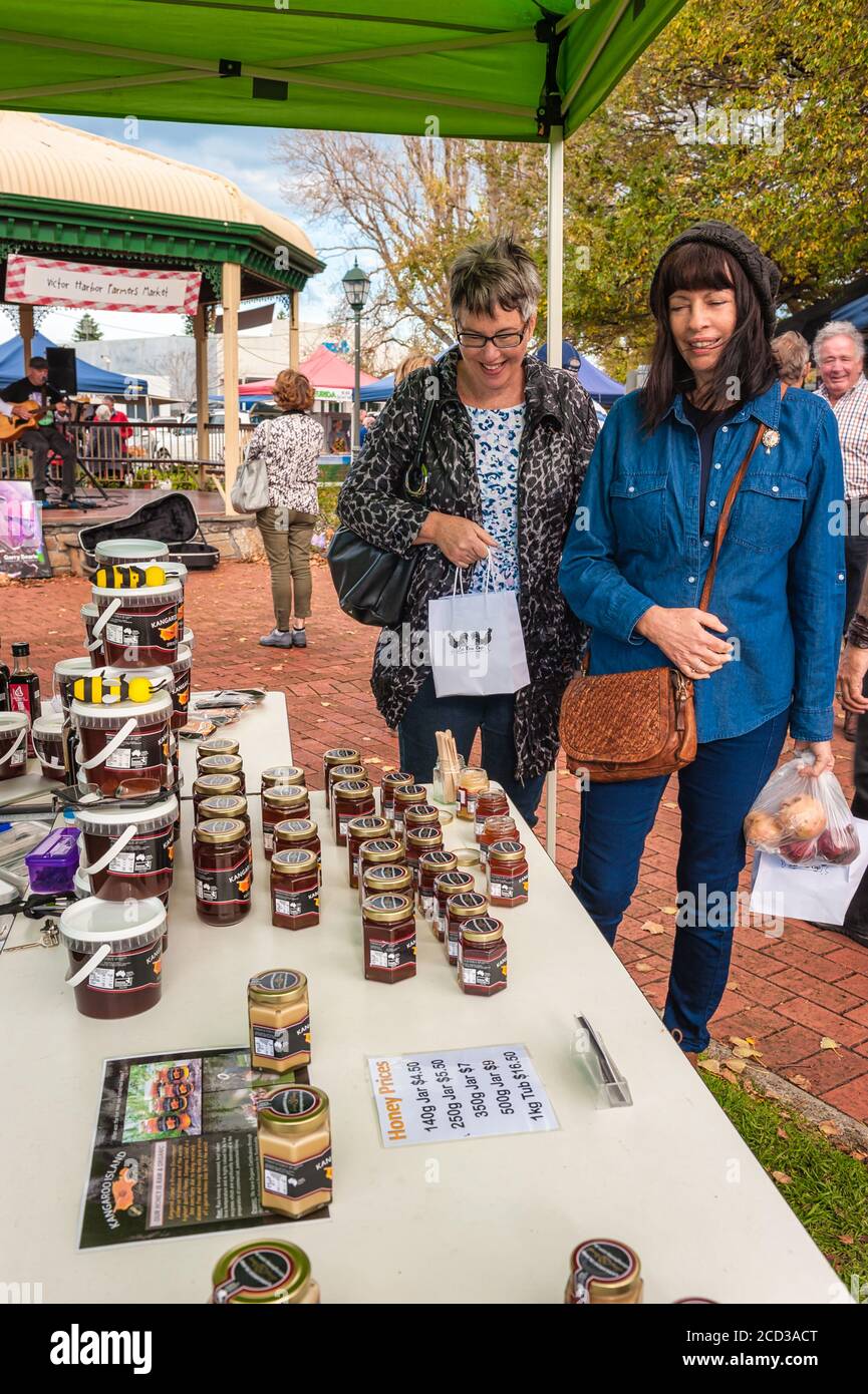 Zwei Freunde lächeln und teilen ein Einkaufserlebnis, während sie zum nächsten Stand am Victor Harbor Farmers Market in Südaustralien gehen. Stockfoto
