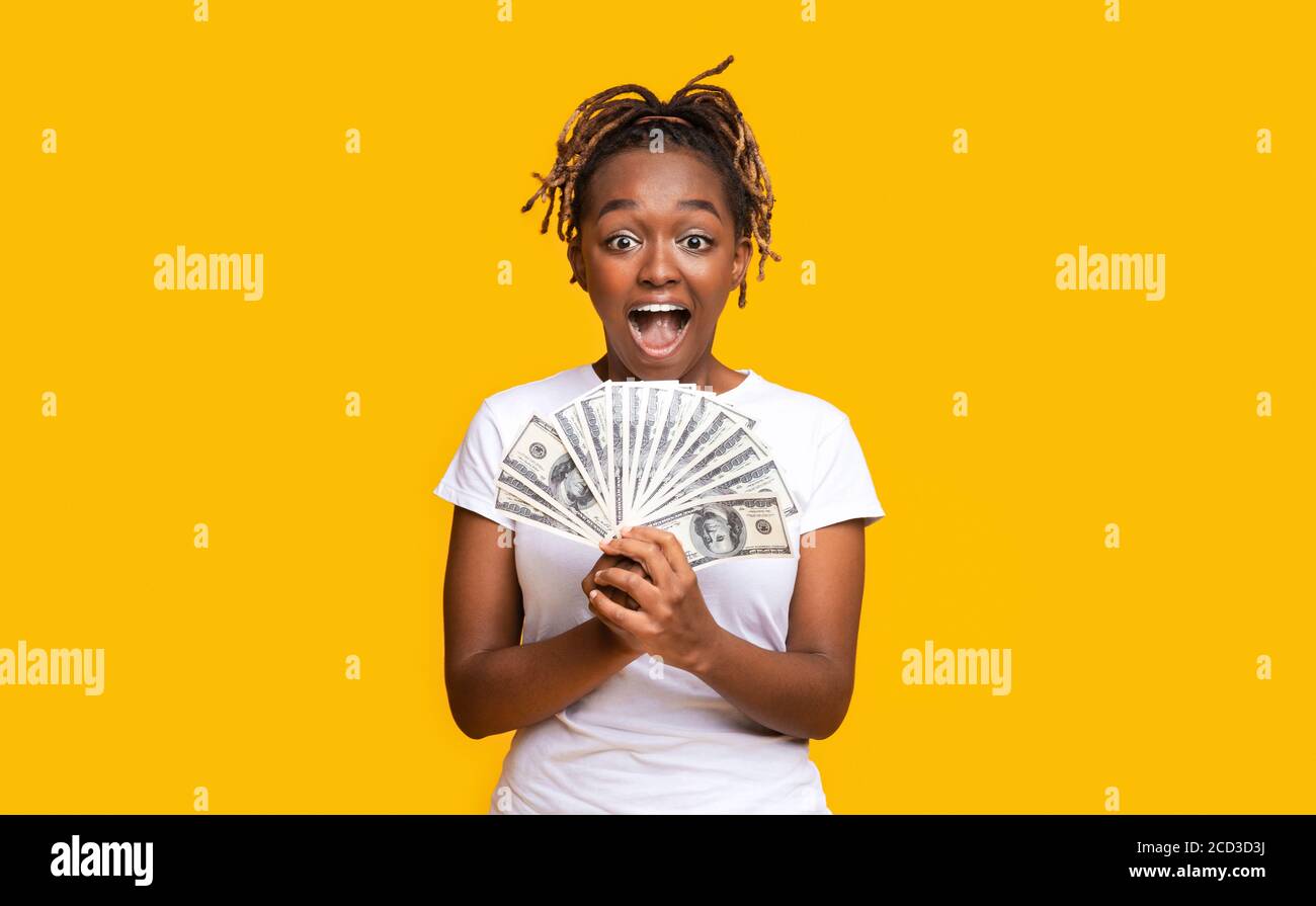 Emotionale schwarze Frau hält Geld auf gelbem Hintergrund Stockfoto