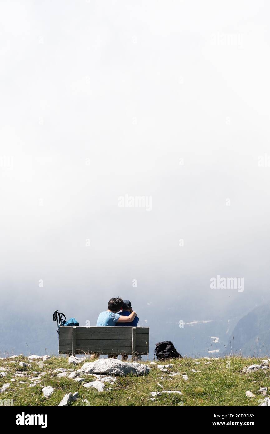 Streicheln Wanderpaar entspannen auf einer Bank und genießen Sie die Aussicht auf dem Gipfel des Berges mit Blick auf Tal im Nebel. Zweisamkeit, Liebe, Wandern und Relaxat Stockfoto