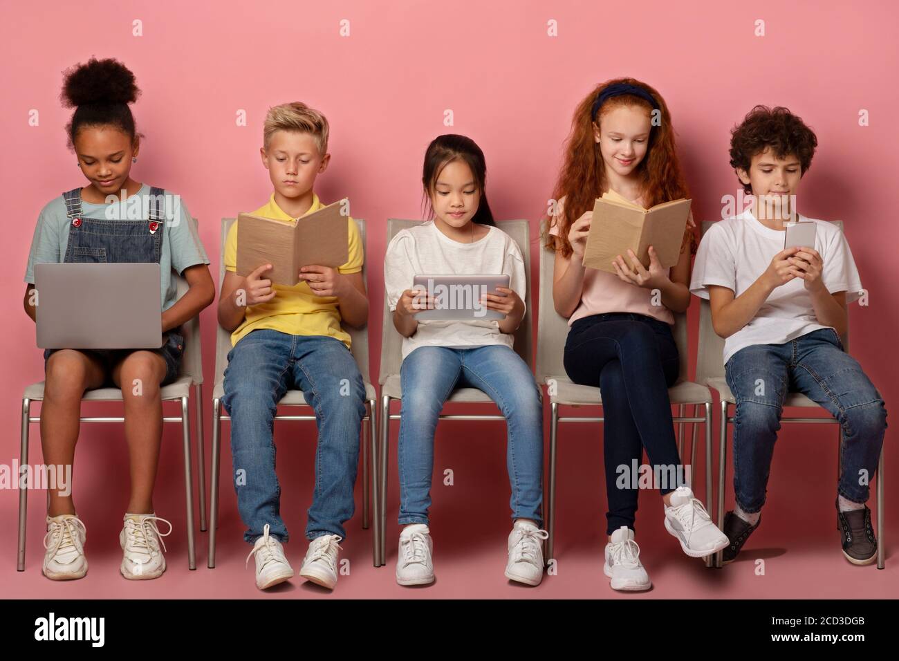 E-Learning-Konzept. Fokussierte verschiedene Schüler mit Gadgets und Lernmaterialien auf Stühlen über rosa Hintergrund sitzen Stockfoto