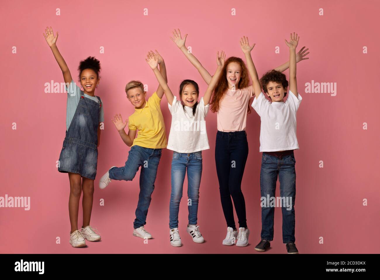 Fröhliche multiethnische Schüler heben ihre Hände auf rosa Hintergrund Stockfoto