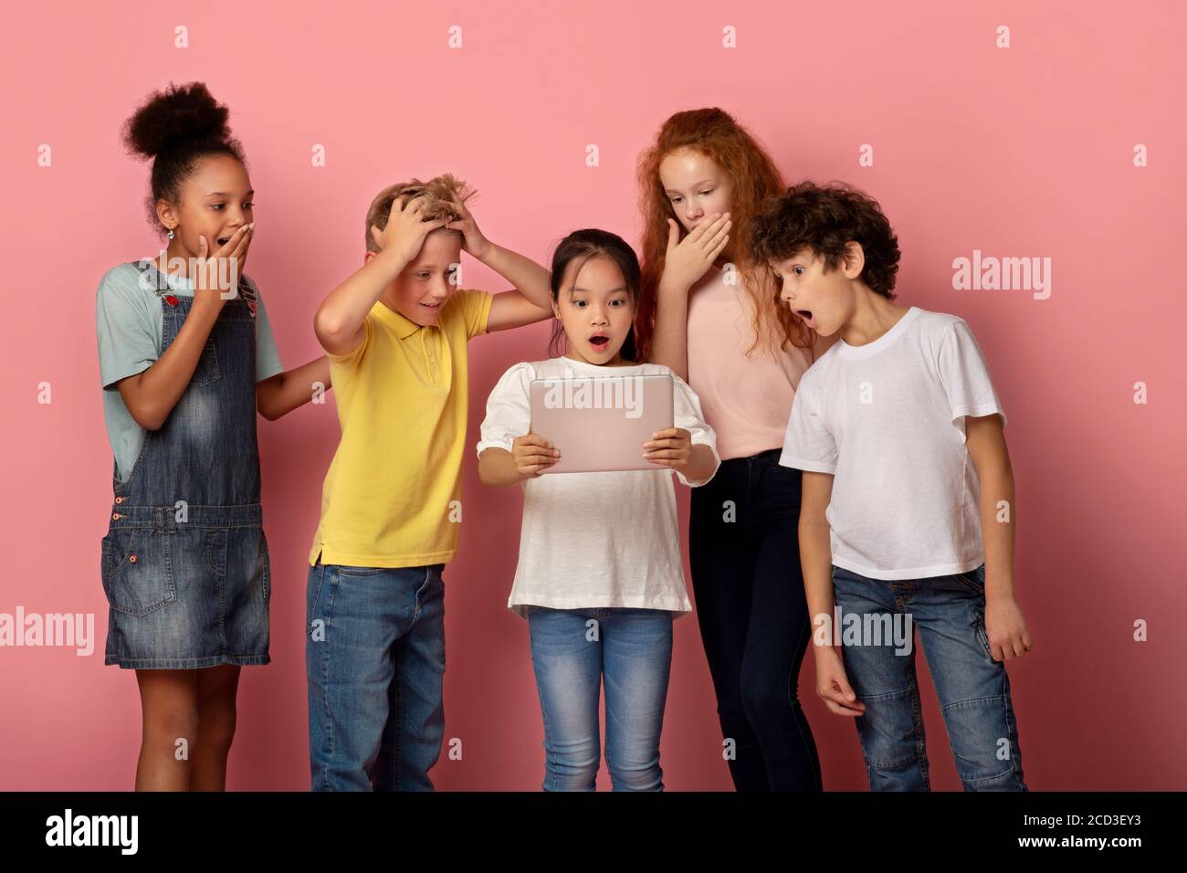 Gruppe von überraschten multirassischen Freunden beobachten etwas auf Tablet-Computer zusammen, rosa Hintergrund Stockfoto