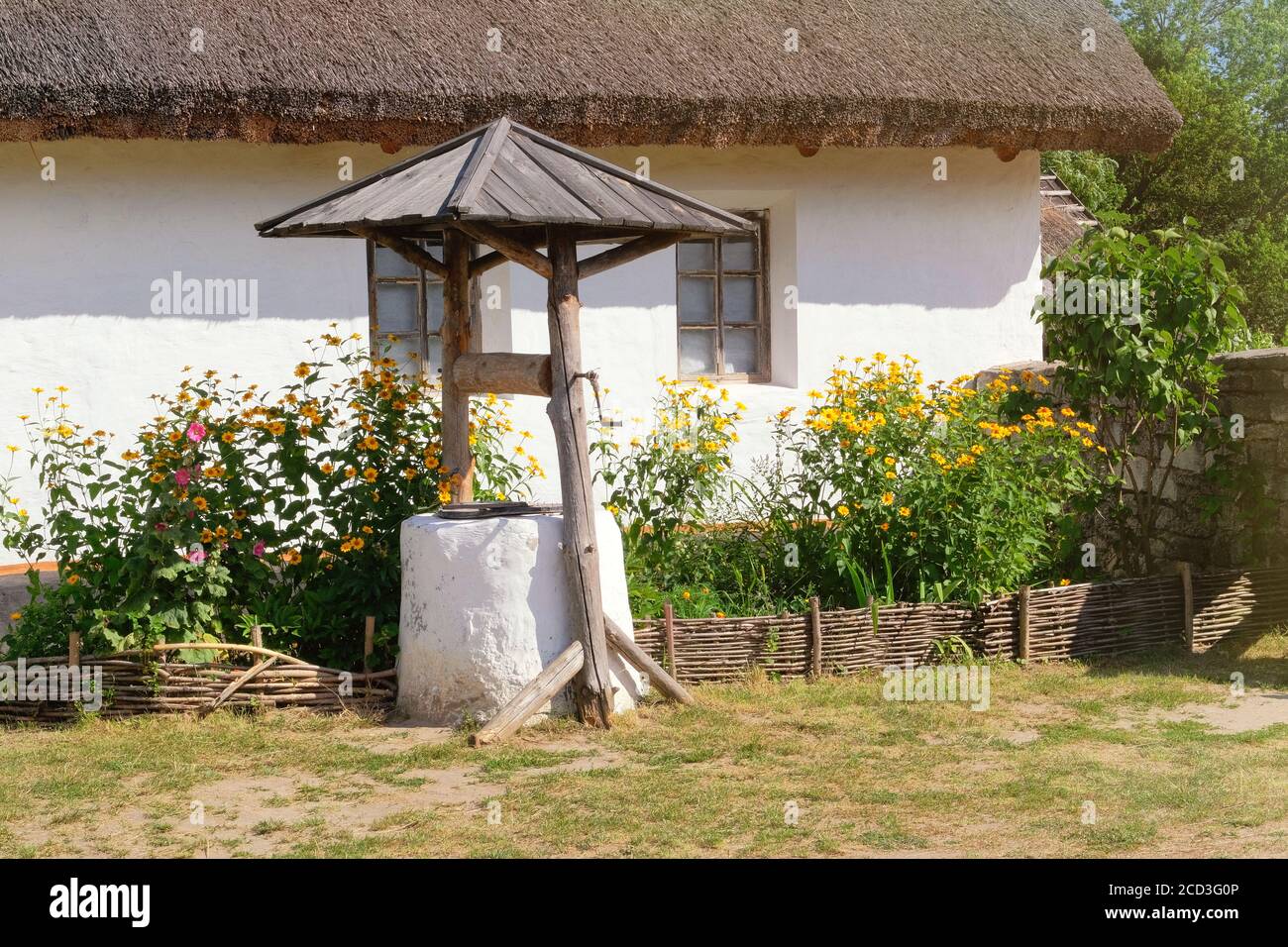 Alter Brunnen in der Nähe einer ländlichen Hütte mit weiß getünchten Wänden. Dorf bewahrt rustikale Traditionen und Kultur. Stockfoto
