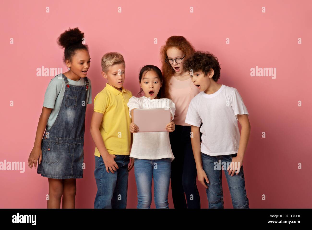 Schockiert Kinder starren in Tablet-Bildschirm zusammen, erstaunt über etwas, rosa Hintergrund Stockfoto