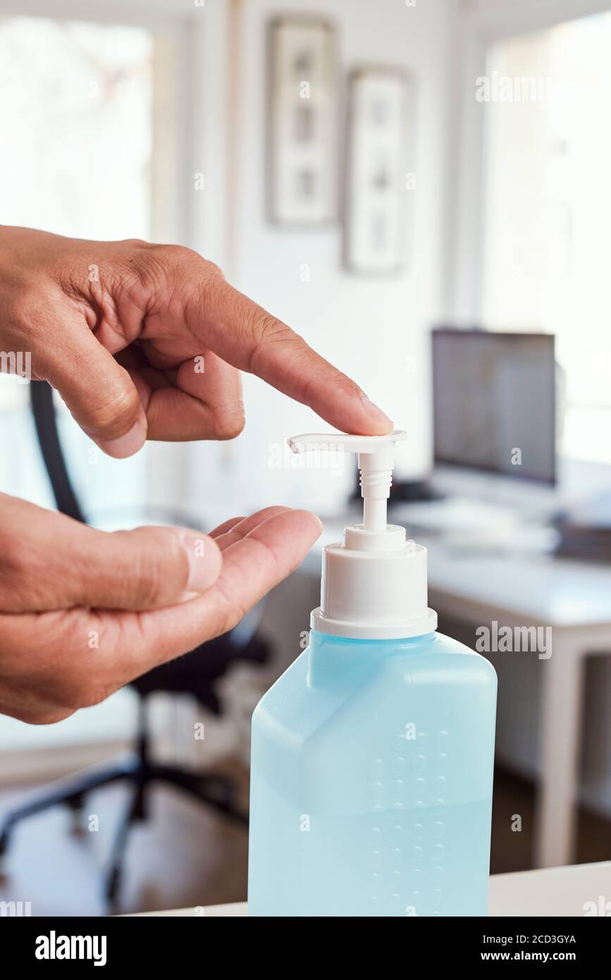 Nahaufnahme eines jungen Kaukasiers in seinem Büro, der seine Hände mit einem Händedesinfektionsmittel aus einer blauen Flasche vor seinem Schreibtisch desinfiziert Stockfoto