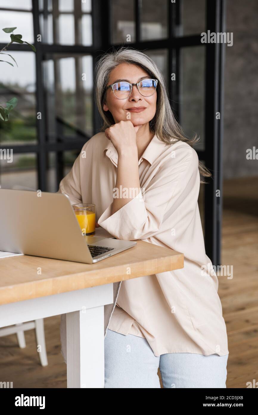 Foto von reifen träumen konzentrierte Geschäftsfrau drinnen zu Hause Mit Laptop-Computer Stockfoto