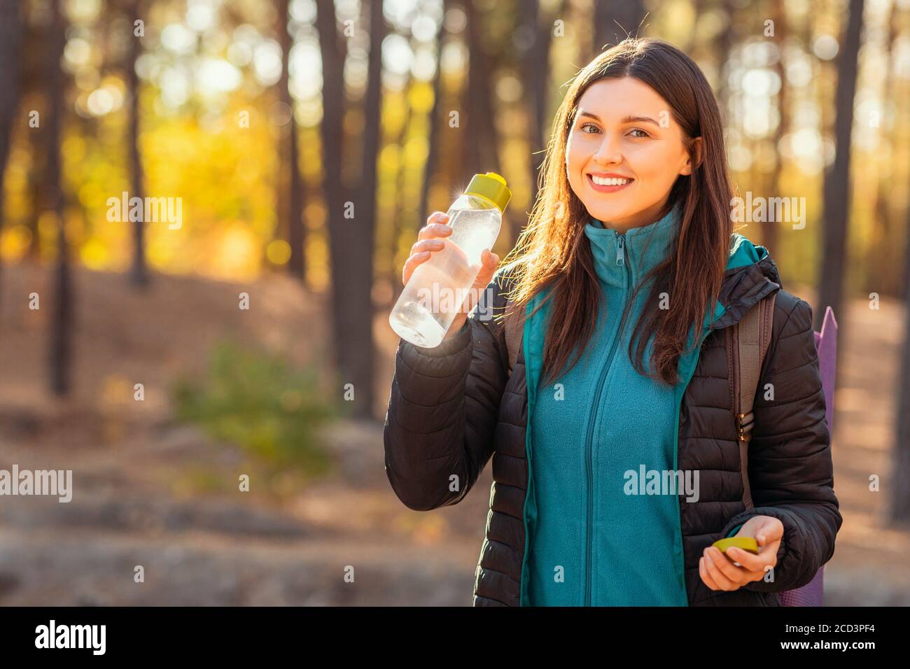 Fröhliche junge Frau Backpacker Trinkwasser im Wald Stockfoto