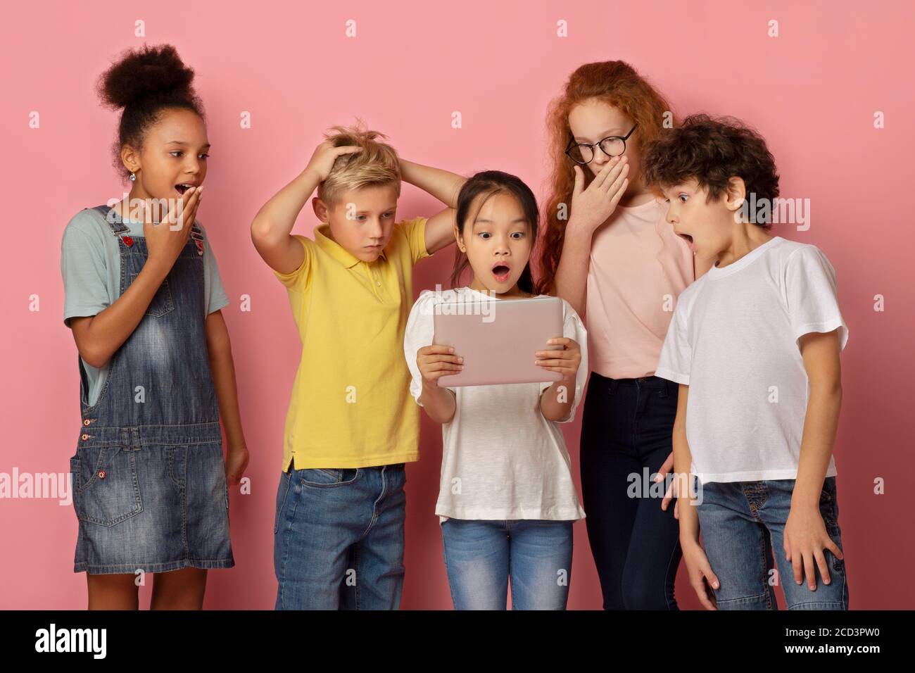 Überrascht Jungen und Mädchen, die zusammen auf Tablet-Computer, Lernen schockierende Nachrichten über rosa Hintergrund Stockfoto