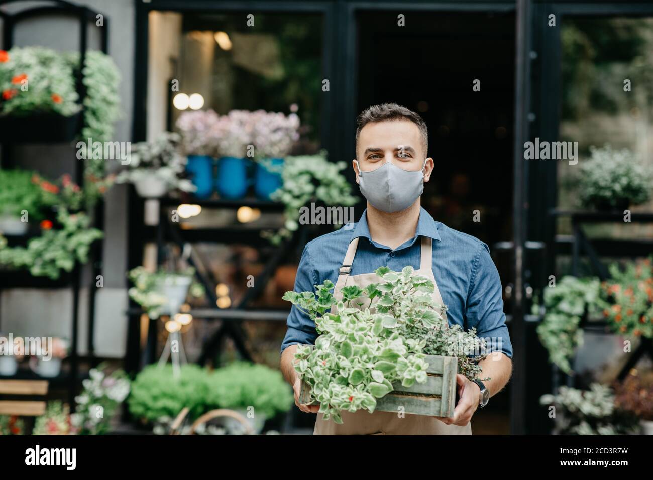 Kleinunternehmen und Beginn des Arbeitstages. Mann in Schutzmaske nimmt Kasten der Pflanzen draußen Stockfoto
