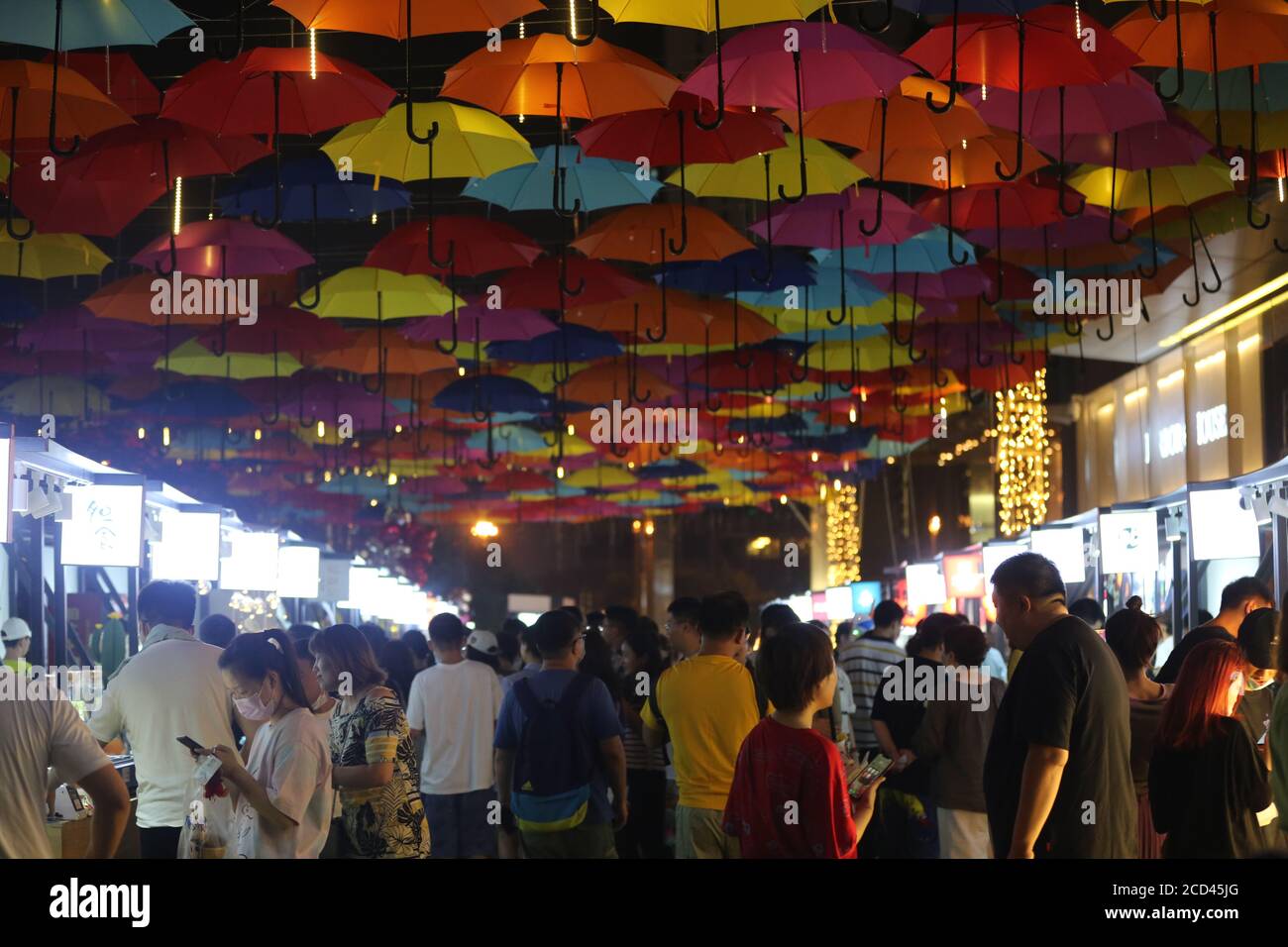 Die Menschen gehen unter einem Korridor, der mit bunten Regenschirmen geschmückt ist und den Nachtmarkt in Shenyang, im nordöstlichen Teil von Liao, ankurbeln soll Stockfoto