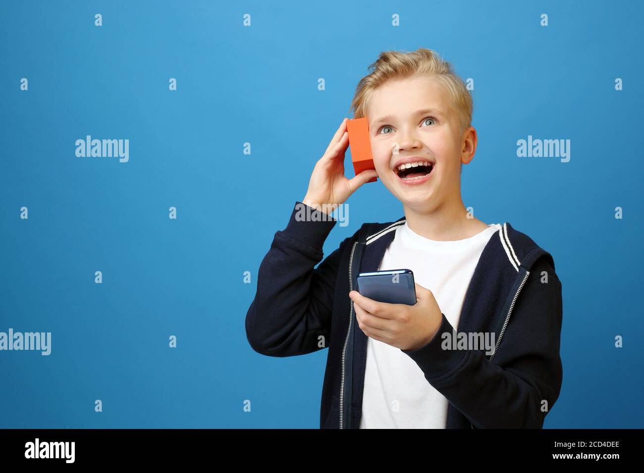 Junge hört Musik aus dem Lautsprecher und dem Telefon. Porträt eines Kindes auf einem farbigen blauen Hintergrund. Emotionen und Gefühle, die durch Faci ausgedrückt werden Stockfoto