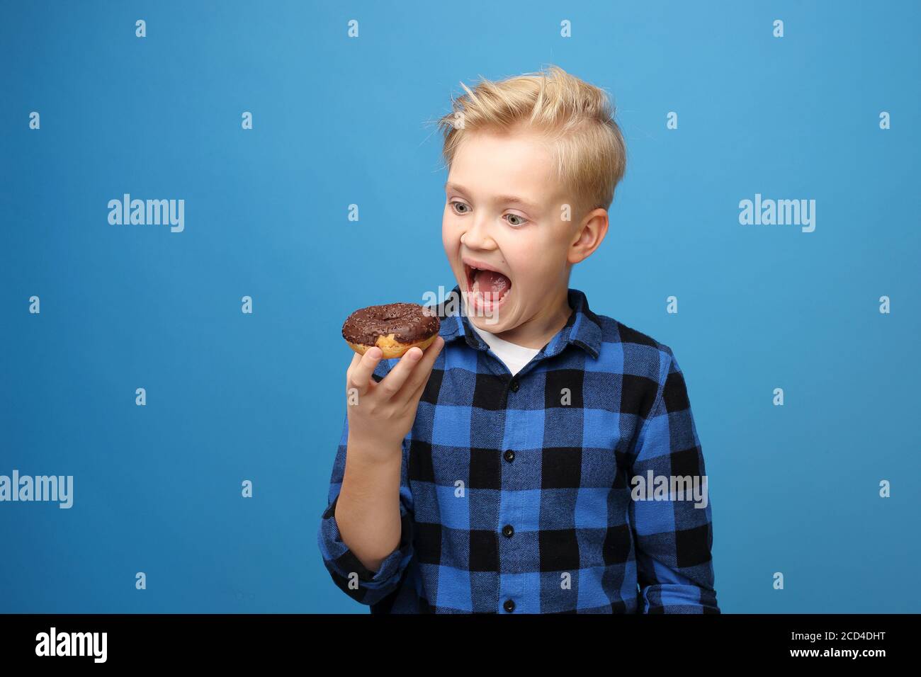 Süßigkeiten, lächelnder Junge mit einem süßen Donut. Fröhlicher Junge, der ein süßes Dessert isst, lächelnder Junge auf blauem Hintergrund Stockfoto