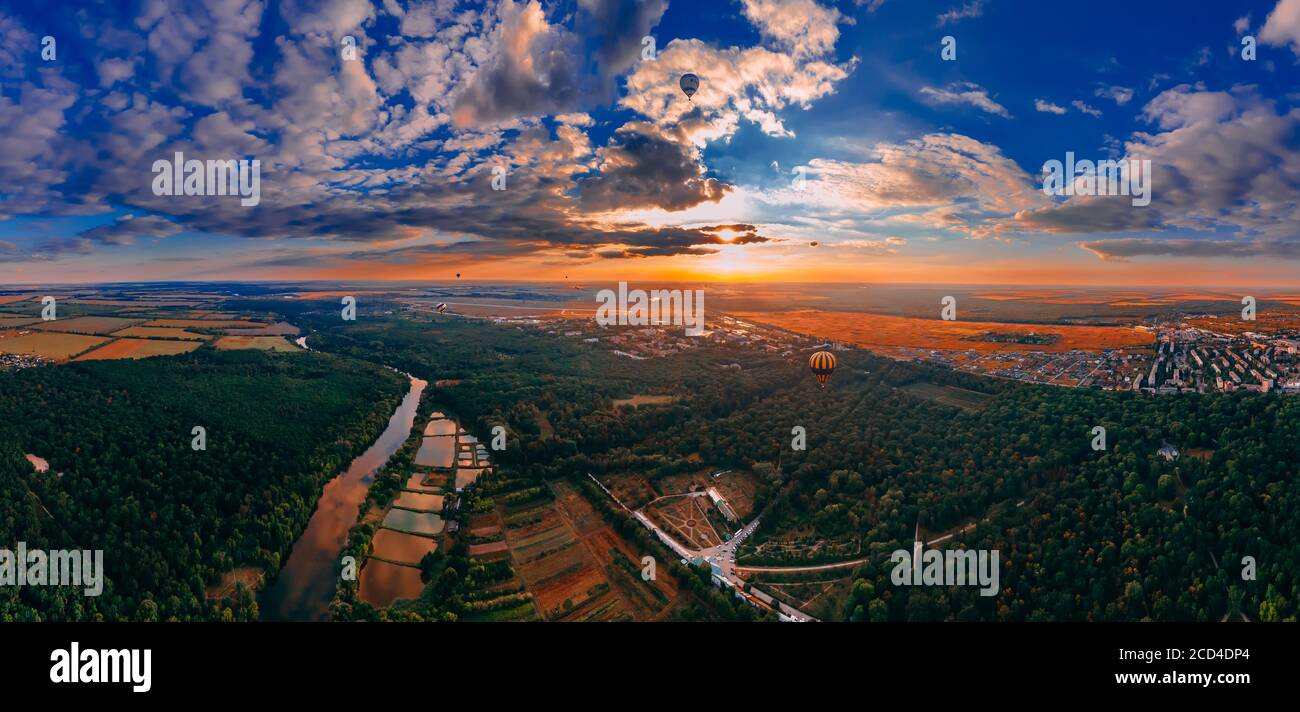 Panorama-Luftbild der bunten Heißluftballons fliegen über Park und Fluss in der kleinen europäischen Stadt bei Sonnenuntergang im Sommer, Kiew Region, Ukraine Stockfoto