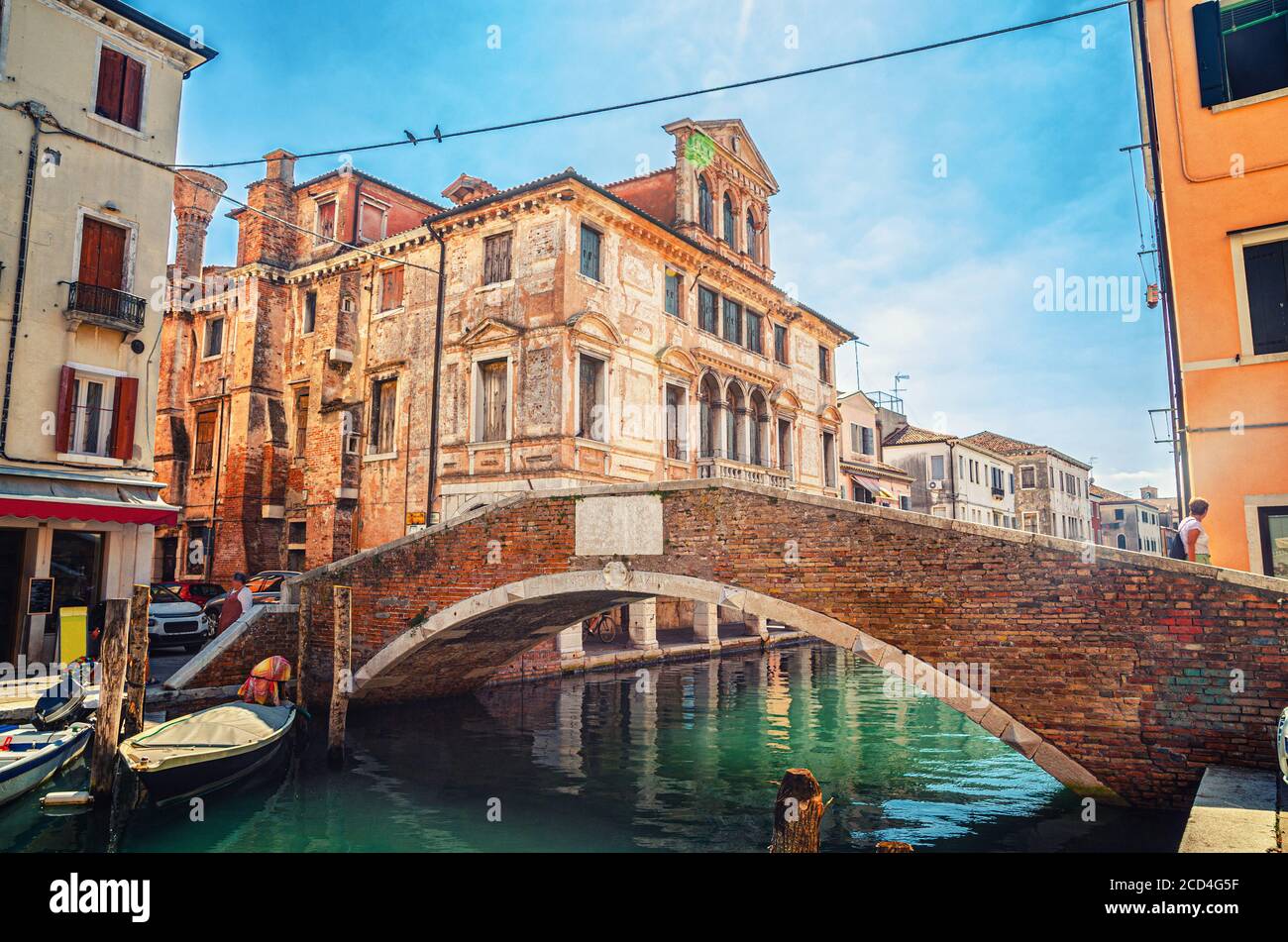 Brücke aus Stein Ponte Caneva über Vena Wasserkanal mit festgezurrenen Booten und altem Gebäude im historischen Zentrum von Chioggia Stadt, blauer Himmel Hintergrund im Sommertag, Region Venetien, Norditalien Stockfoto