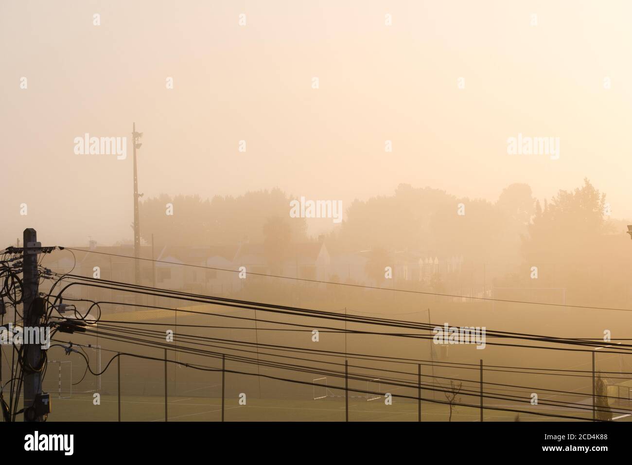 Nebel von der Sonne in goldenen Tönen in einem Stadt mit Häusern und Bäumen im Hintergrund und elektrische Kabel in der Vorderseite Stockfoto