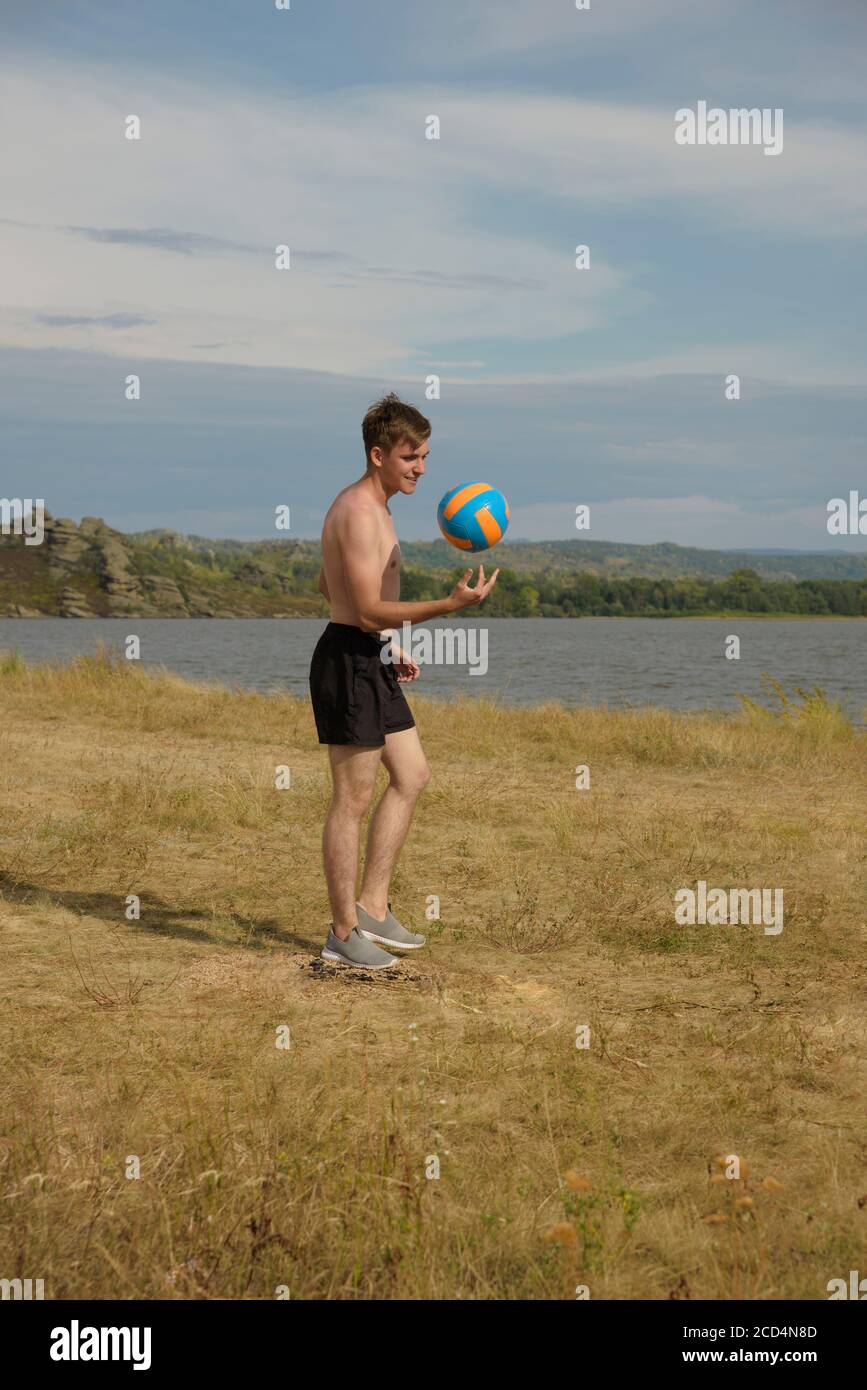 Ein junger Mann in schwarzen Shorts wirft einen Volleyball. Stockfoto