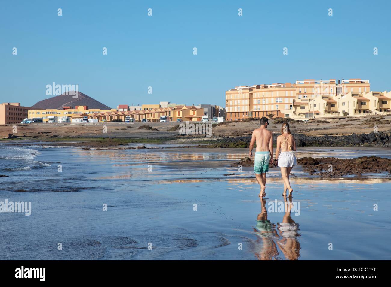 Mann und Frau schlendern am feinen Strand mit ruhigen Wellen und vulkanischem Sand an der Playa de la Jaquita, in der Nähe von El Medano, an einem frühen Morgen, Teneriffa Stockfoto