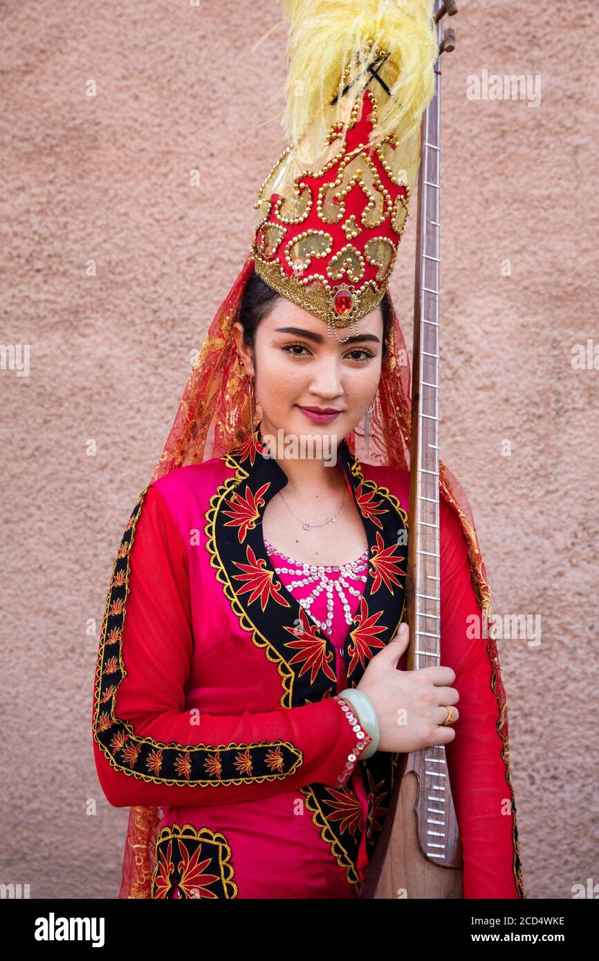 Uiguren Mädchen in roten traditionellen Kleid mit Satar, chinesische langhalsige gebeugte Laute in der Stadt Kashgar / Kashi / Kasjgar, Xinjiang, China Stockfoto