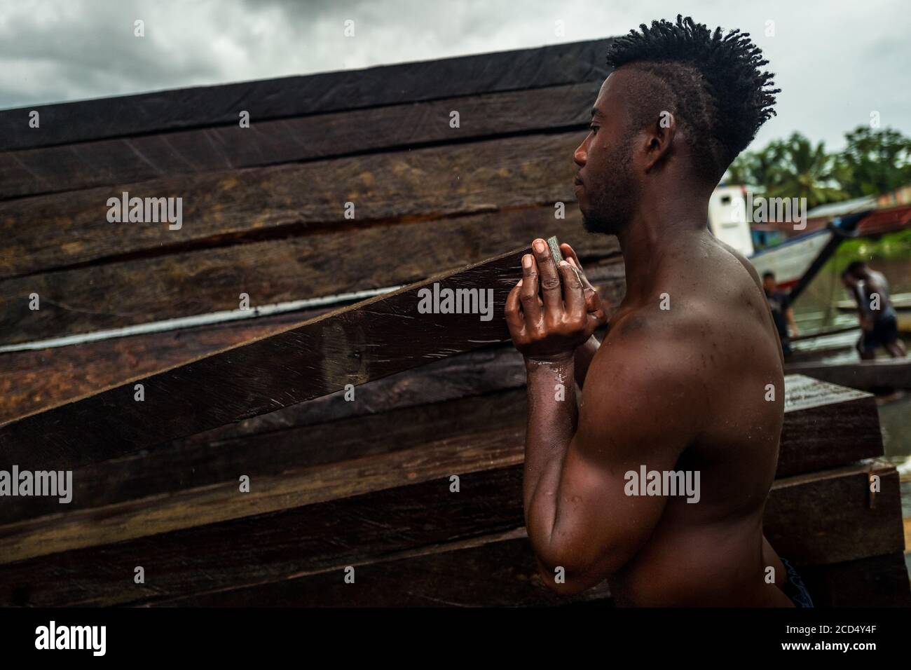 Ein afro-kolumbianischer Träger hebt ein grobes Schnittholz, das aus dem pazifischen Regenwald gewonnen wird, während des Holztransports im Hafen von Turbo, Kolumbien. Stockfoto