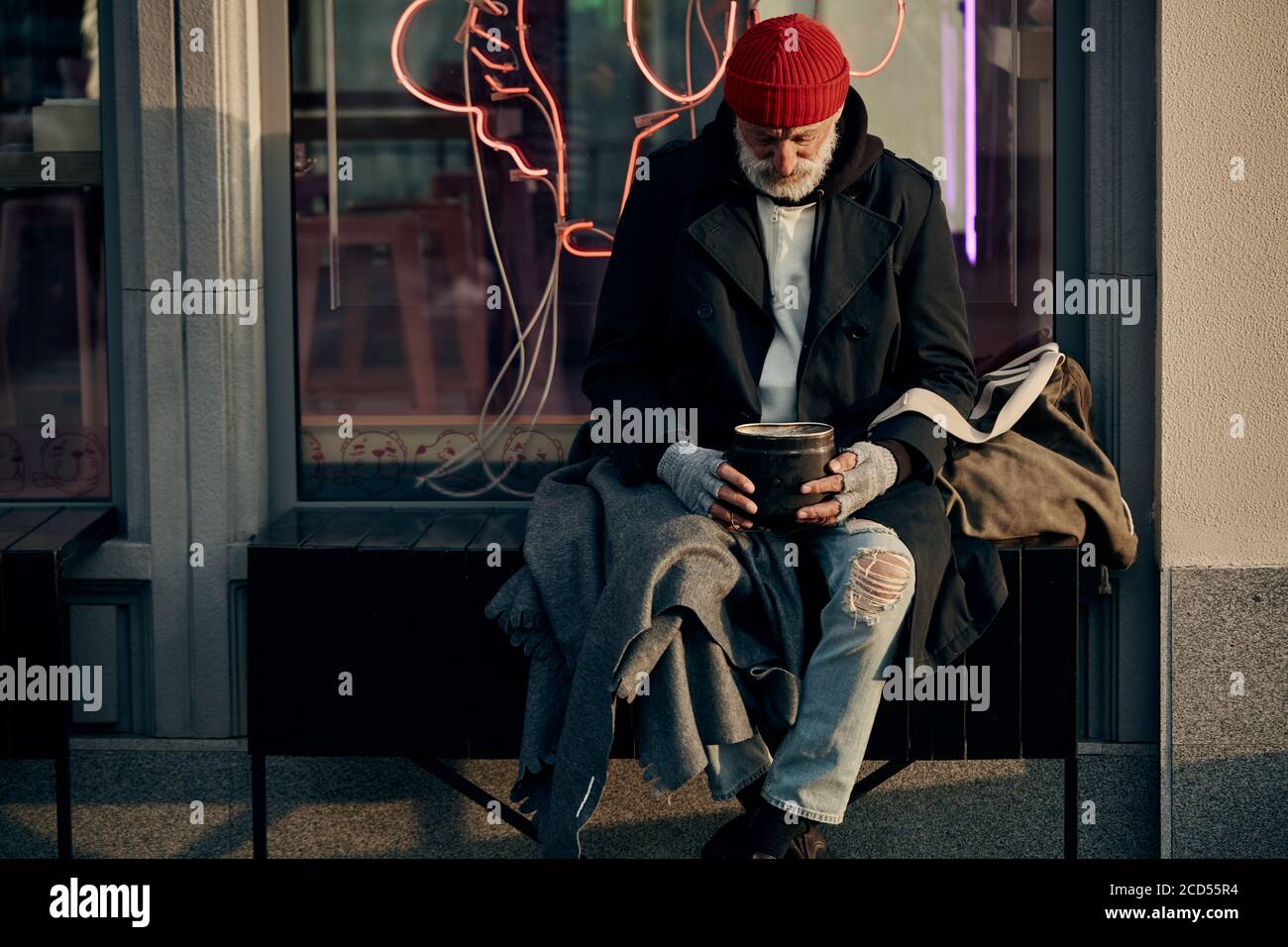 Trauriger vagrant Mann bitten um etwas Geld Spenden von den Bürgern, modernes Café hinter ihm. Armut, Hunger, Hoffnung Stockfoto