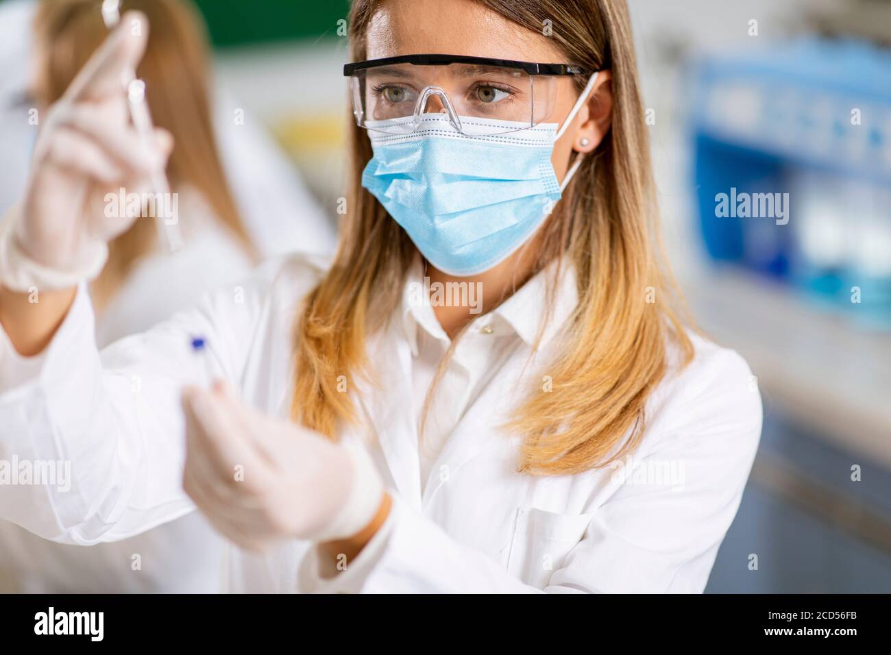 Frau Arzt trägt schützende Gesichtsmaske und Sicherheit googles in Labornadelspritze und Impfstoffflasche für Medikamentenfläschchen Stockfoto