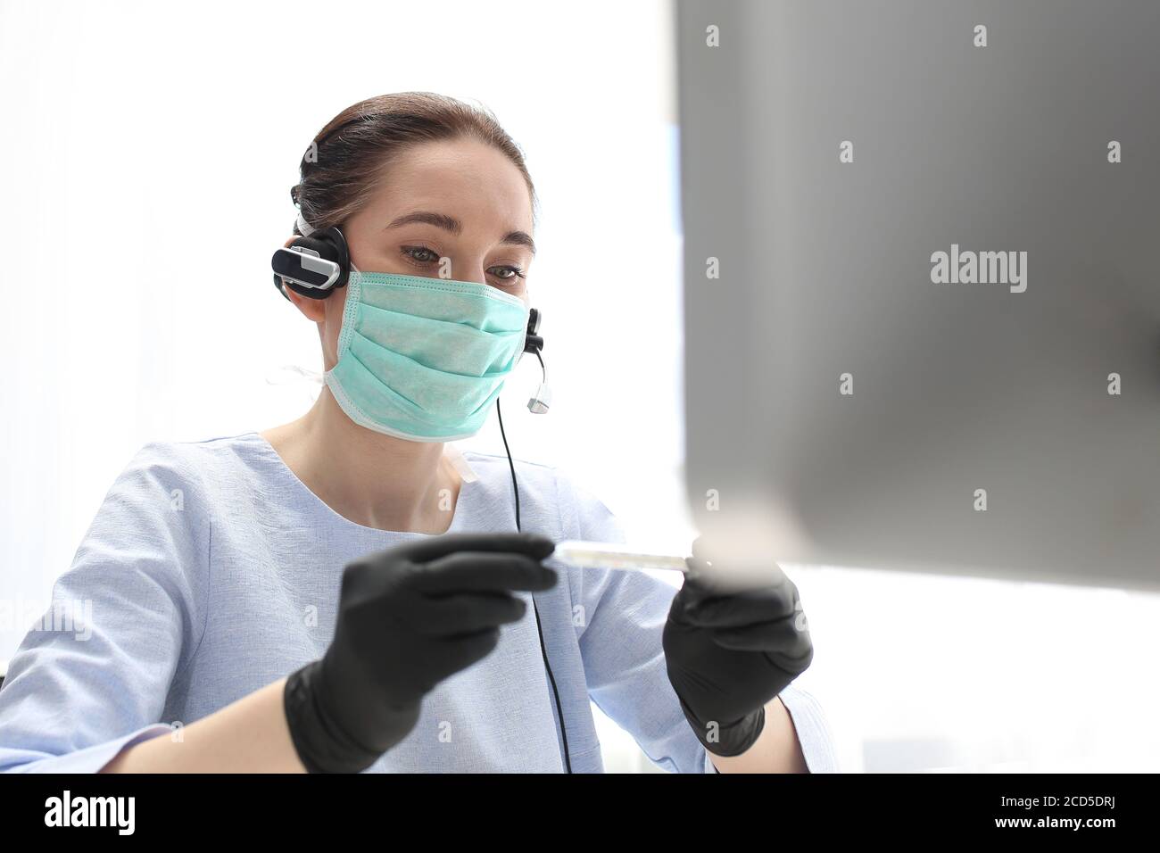 Krankheit bei der Arbeit, erhöhte Temperatur. Eine Frau in einer OP-Maske arbeitet am Computer. Arbeiten während der Pest. H Stockfoto