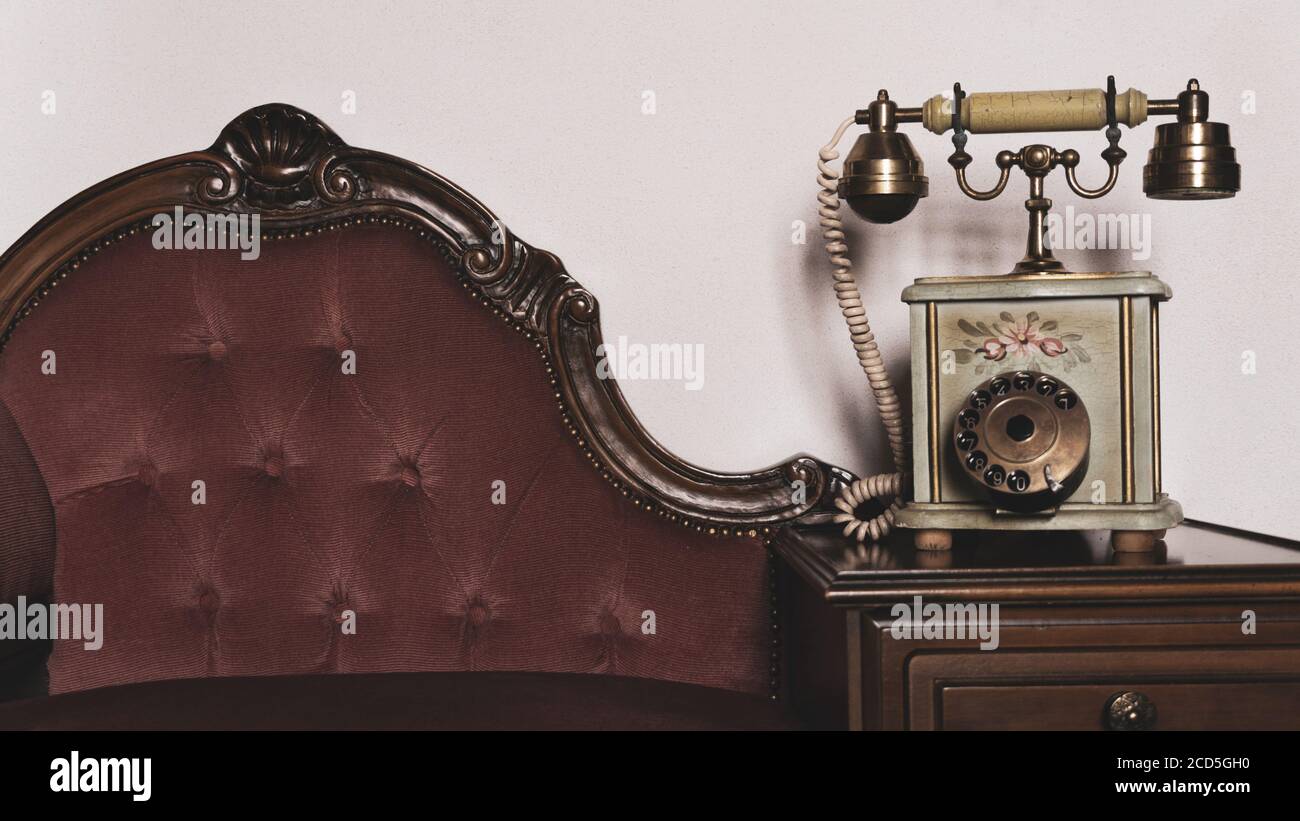 Elegantes Vintage altes Telefon auf elegantem gepolstertem Holzsofa gegen Weiße Wand.entspannende antike Zimmer Inneneinrichtung Vintage-Dekoration Stockfoto