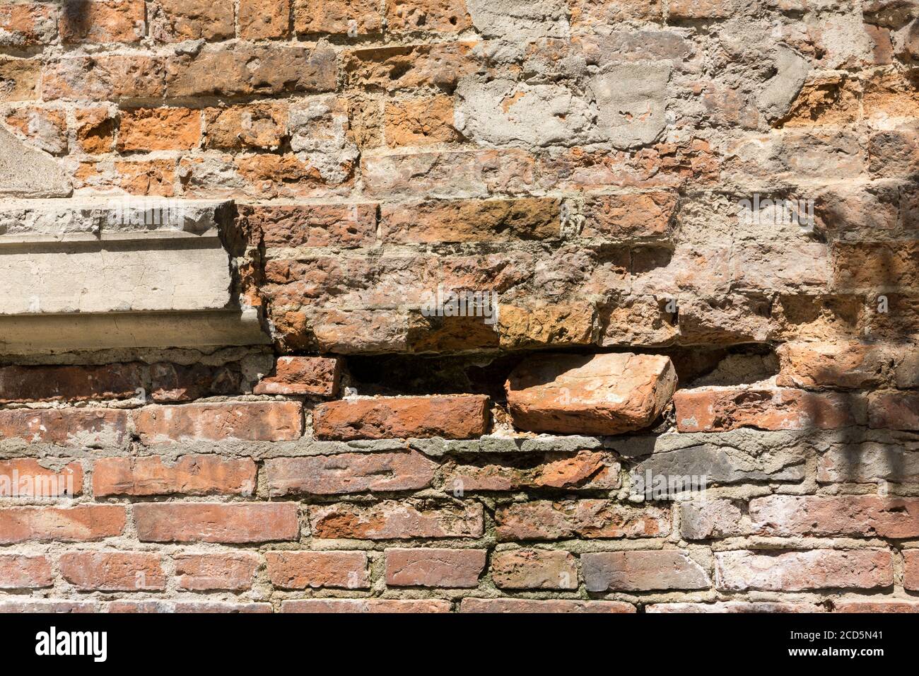 Baufällig mit Schlaglöchern alte Backsteinmauer des Gebäudes, aus rotem Backstein, aus nächster Nähe. Hintergrund oder Textur. Stockfoto