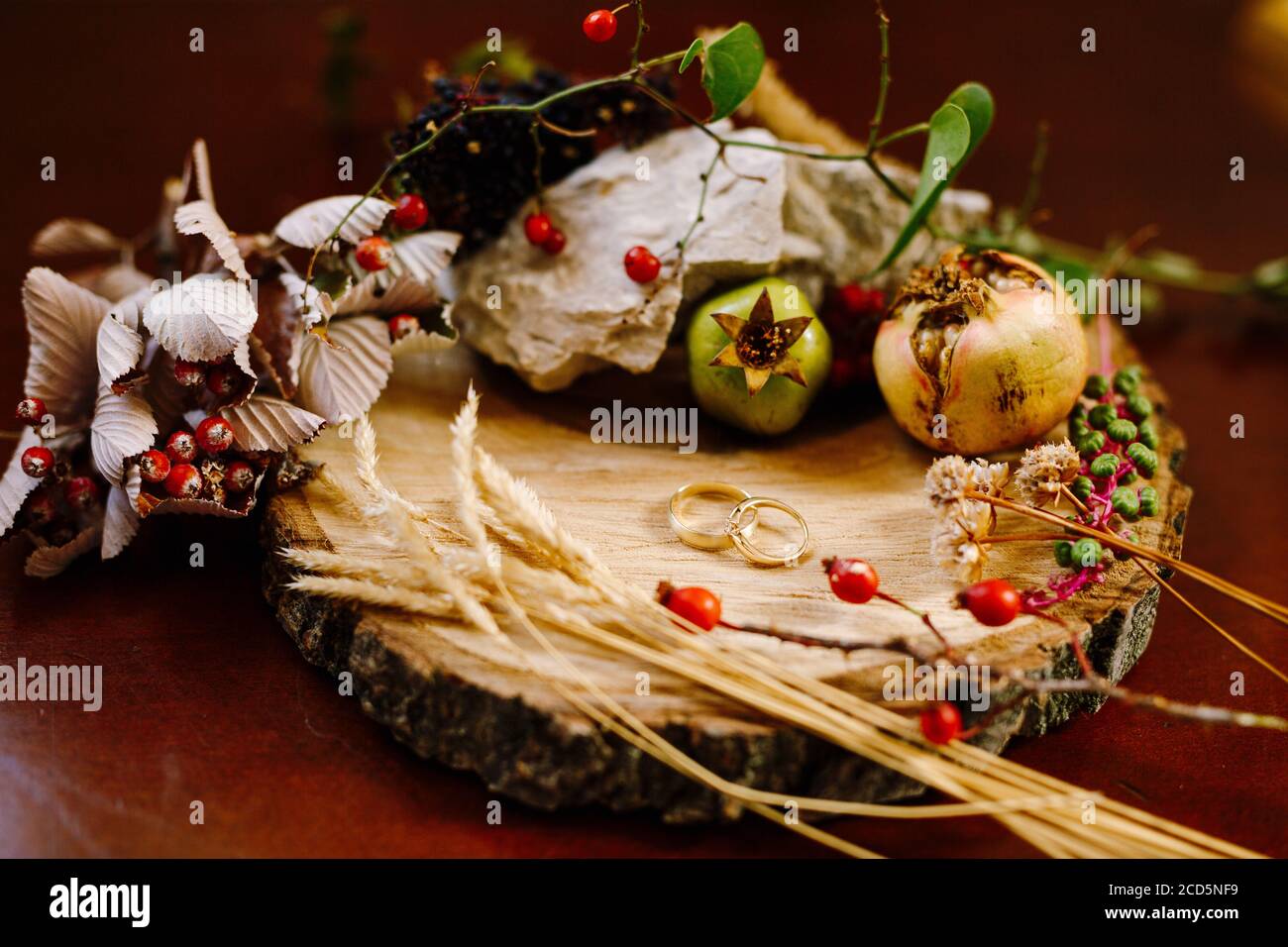 Kleine Granatapfelfrüchte, Hagebutten und Dornen um goldene Eheringe auf einem Holzbrett. Stockfoto