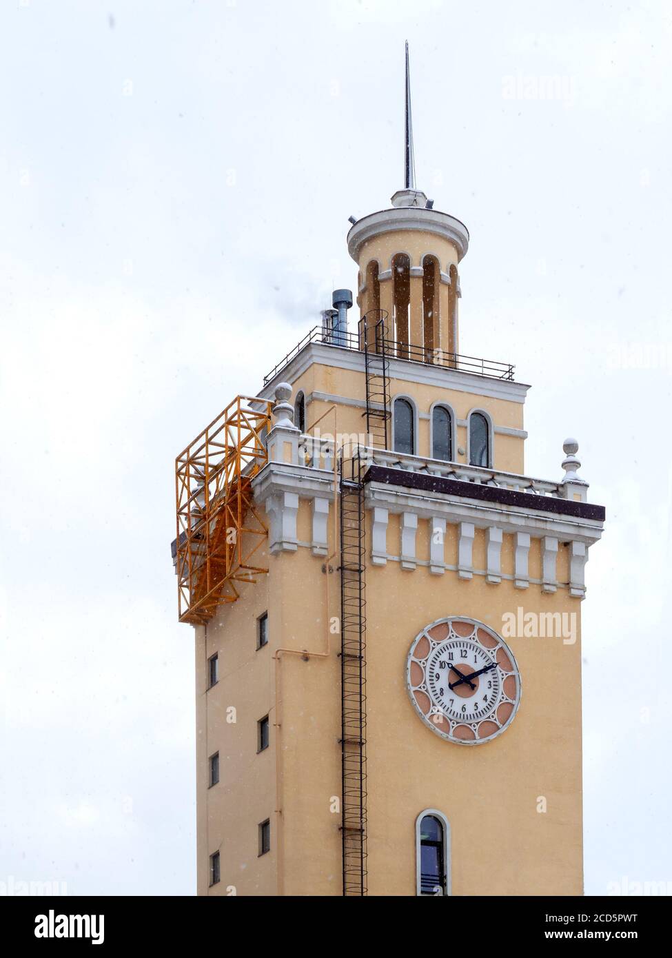 Beigefarbener Uhrenturm, Kirchturm, kleine Fenster und eine dünne lange Treppe, gegen den Himmel Stockfoto