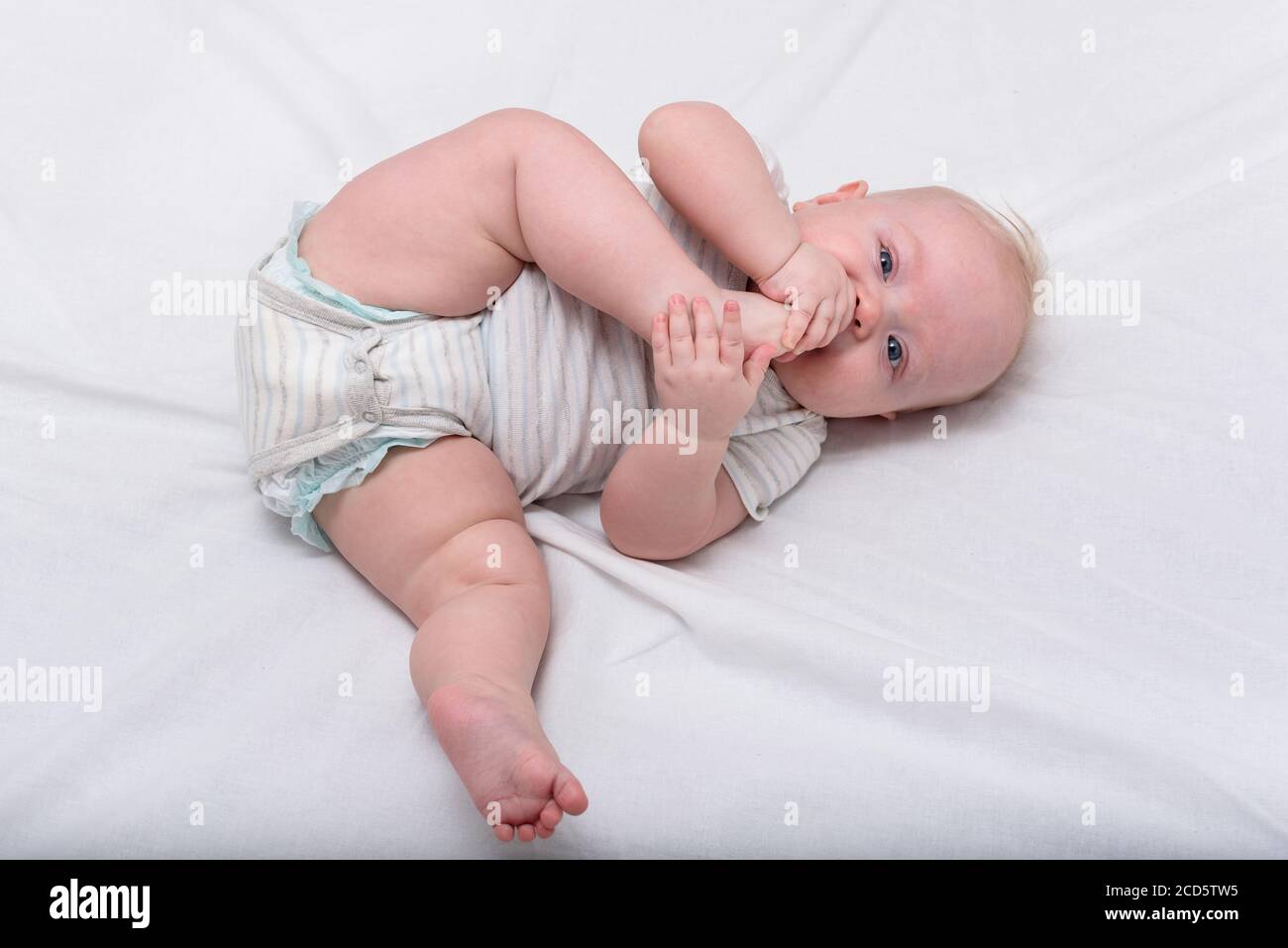 Kleines Baby knabbert seinen Fuß auf weißem Bett. Niedliches 3 Monate Baby.  Gymnastik für das Neugeborene Stockfotografie - Alamy