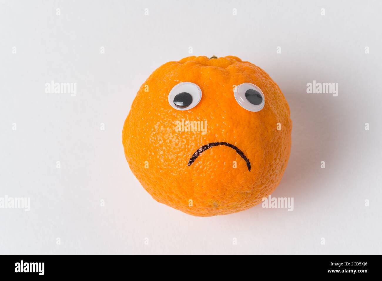 Orangefarbenes Smiley auf weißem Hintergrund. Orange mit Augen und traurigem Lächeln. Essen mit lustigen Gesichtern Stockfoto