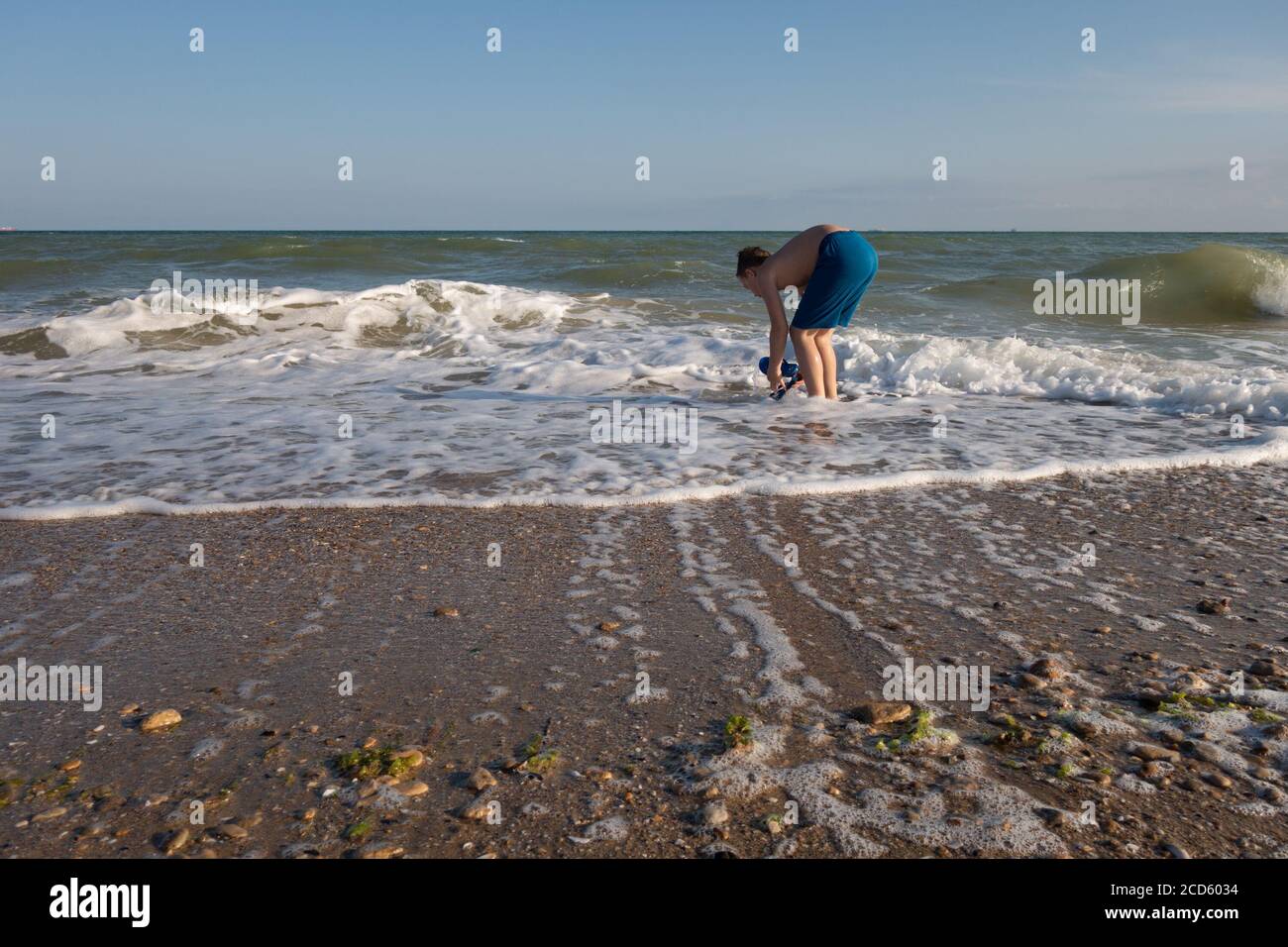 Ein 10-jähriger Junge steht im Meer. Sucht nach Kieselsteinen und versucht, Pfannkuchen zu machen. Stockfoto