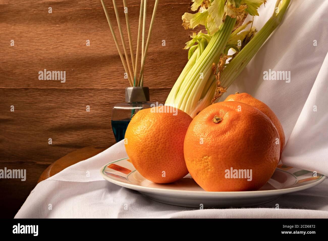 Stillleben von Orangen, Sellerie und blauen Lufterfrischer. Die Nahaufnahme der Orangen sorgt für eine ruhige und kühle Atmosphäre in einem rustikalen Holzambiente. Stockfoto