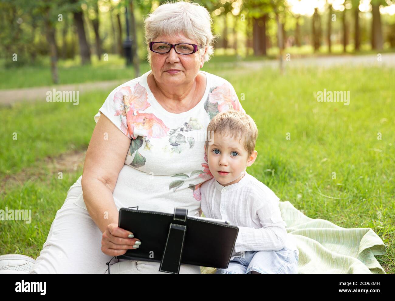 Ältere Frau mit Enkelkind entspannen Sie sich in der Natur und mit modernen Notebook Stockfoto
