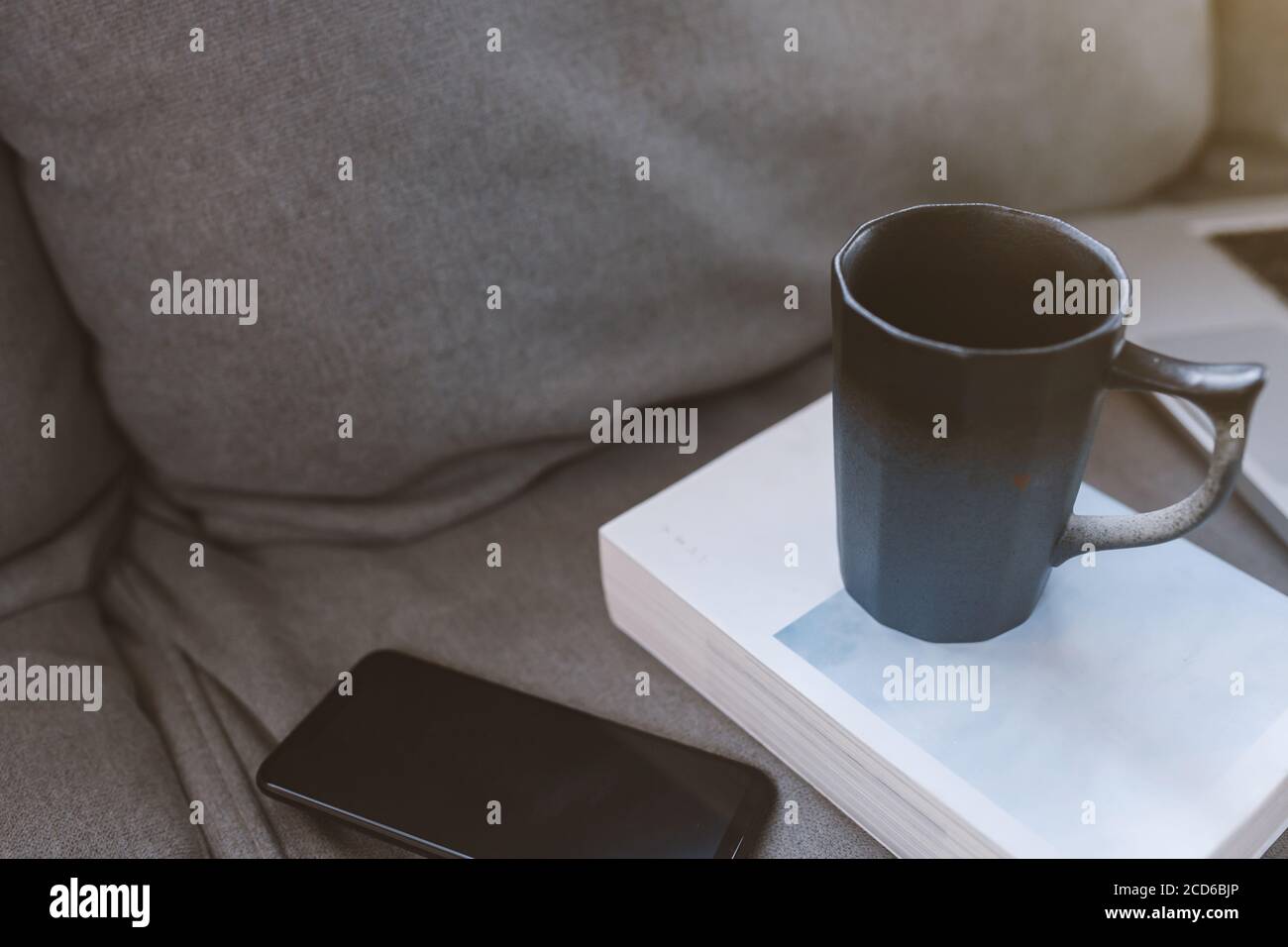 Tasse Kaffee mit Handy auf Sofa im Wohnzimmer. Stockfoto