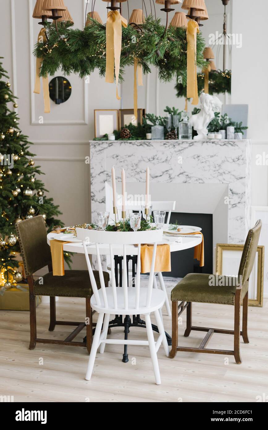 Weihnachtliche Atmosphäre und Komfort im Wohnzimmer. Festlicher Tisch neben dem Marmorkamin und Weihnachtsbaum Stockfoto