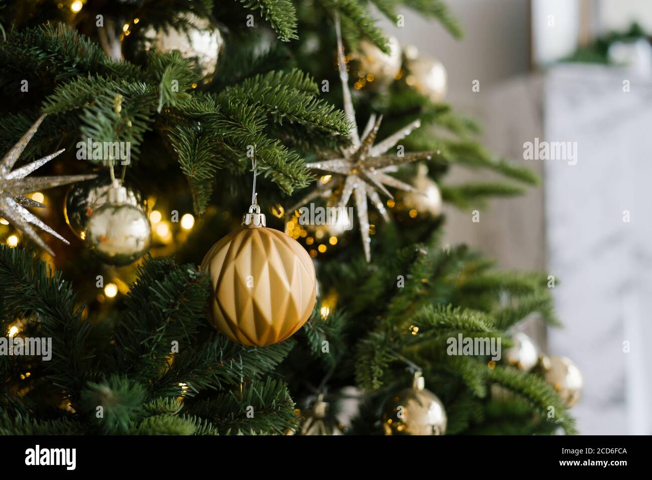 Geschmückter Weihnachtsbaum aus der Nähe. Goldene Kugeln und beleuchtete Girlande mit Taschenlampen. Winterurlaub Licht Dekoration Stockfoto