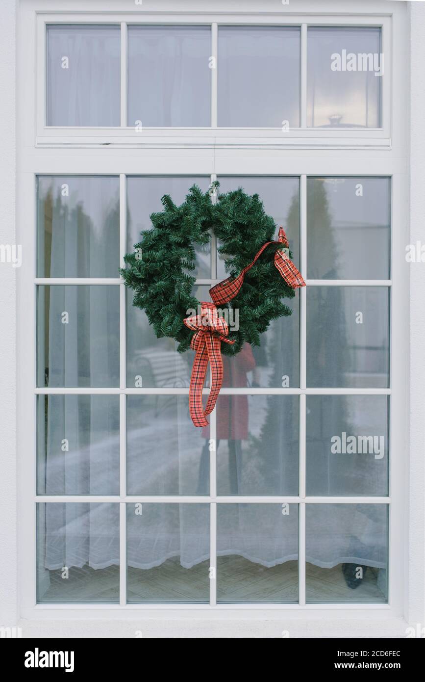 Weihnachtskranz mit roter Schleife auf weißem Fenster In einem privaten Haus Stockfotografie