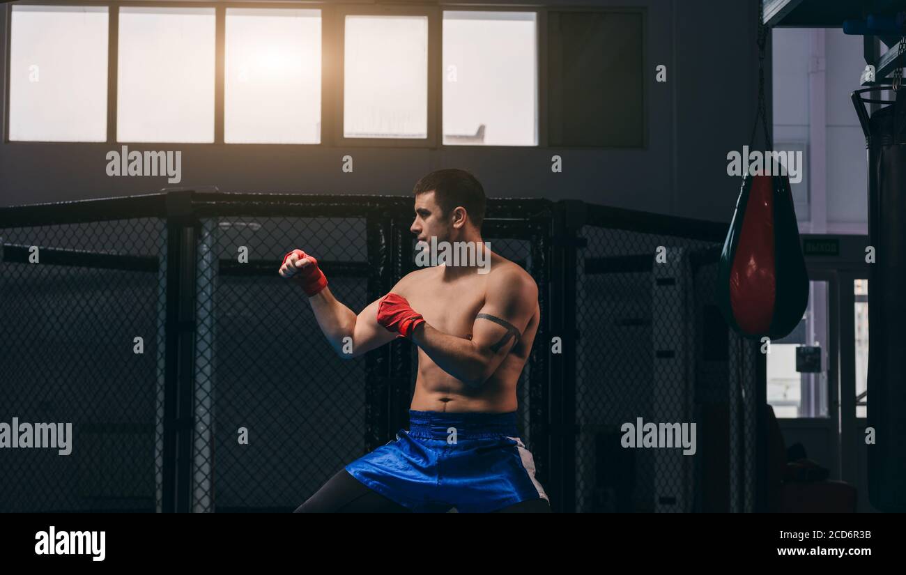 Ein starker, barechested Kickboxer, gemischter Kampfkämpfer in einer Kampfposition, vor einem dunklen Sportzentrum Hintergrund. Stockfoto