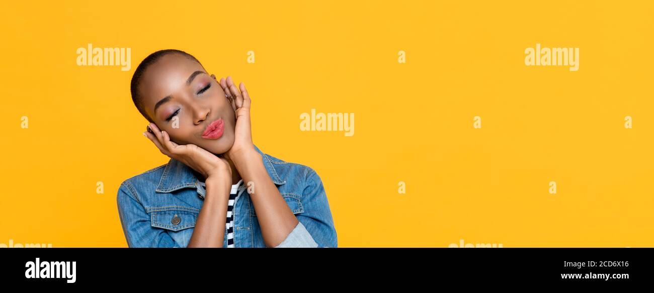 Panoramaporträt einer jungen afroamerikanischen Frau, die die Augen schließt Tagträumen während sie ihr Gesicht berühren isoliert Studio gelben Hintergrund Stockfoto