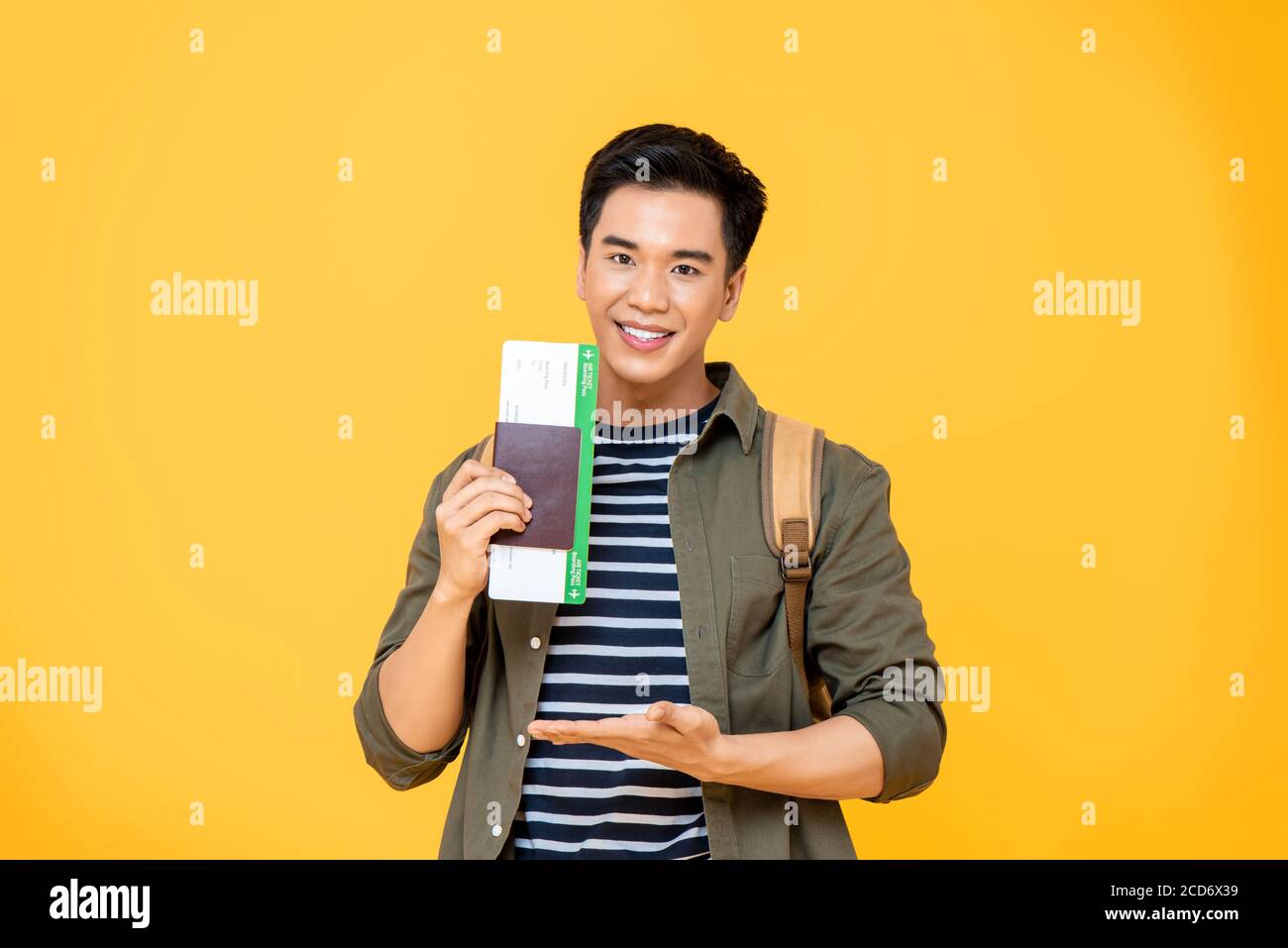 Portrait von lächelnden jungen asiatischen Backpacker Tourist Mann zeigt seine Reisepass mit Bordkarte in offener Handbewegung isoliert auf studio gelb Backgrou Stockfoto