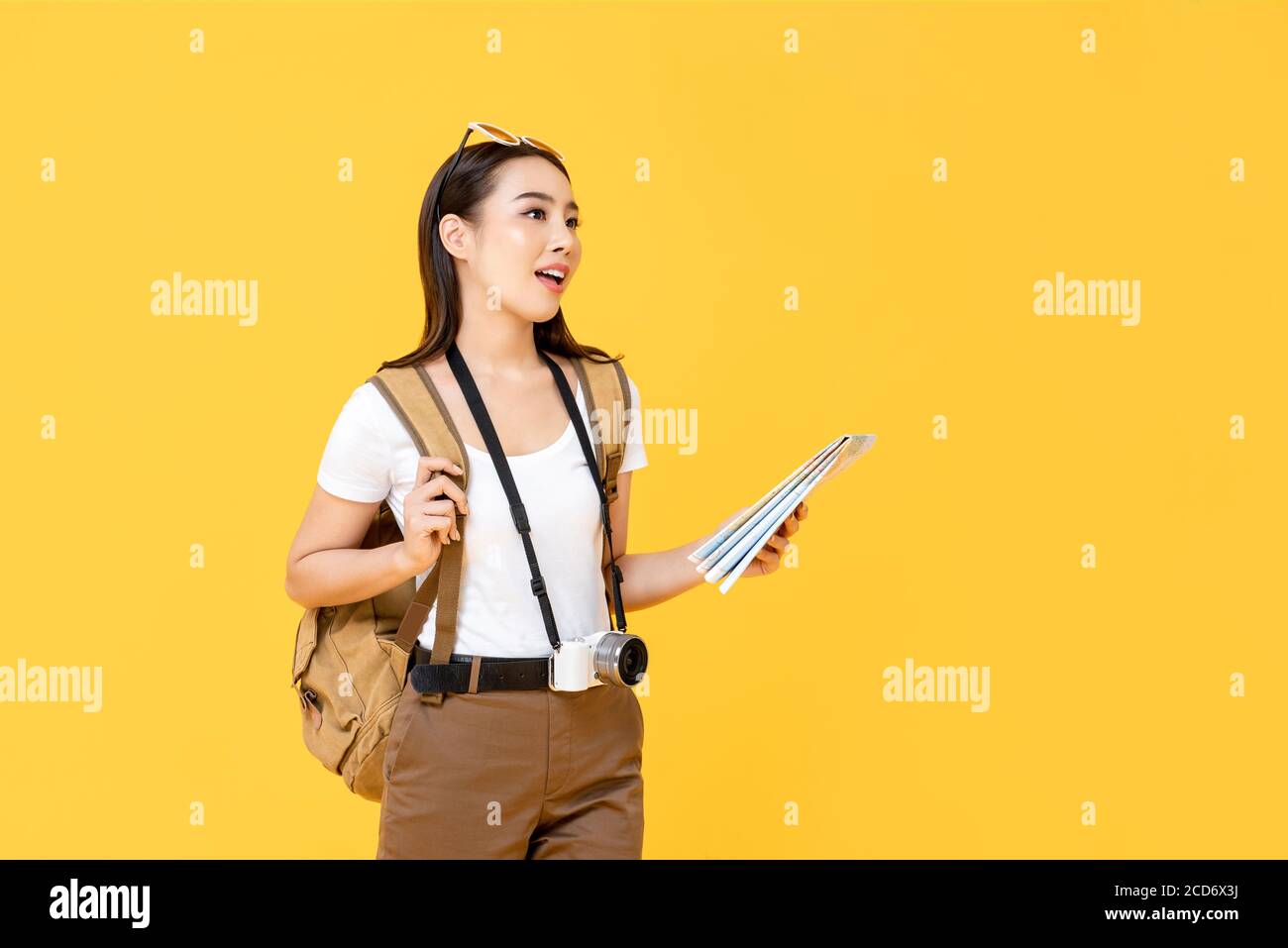 Reisekonzept Porträt der jungen Backpacker asiatische Frau Tourist Holding Karte beim Blick weg in isolierten Studio gelben Hintergrund Stockfoto