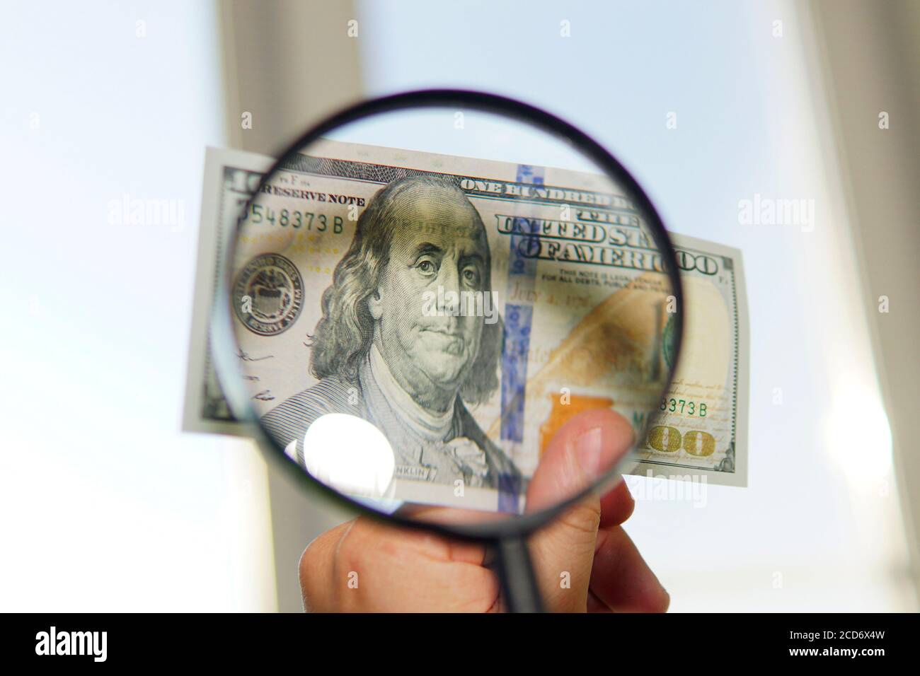 Hundert Dollar Rechnung unter Lupe wird konzeptuell geprüft Foto auf Fensterhintergrund Stockfoto
