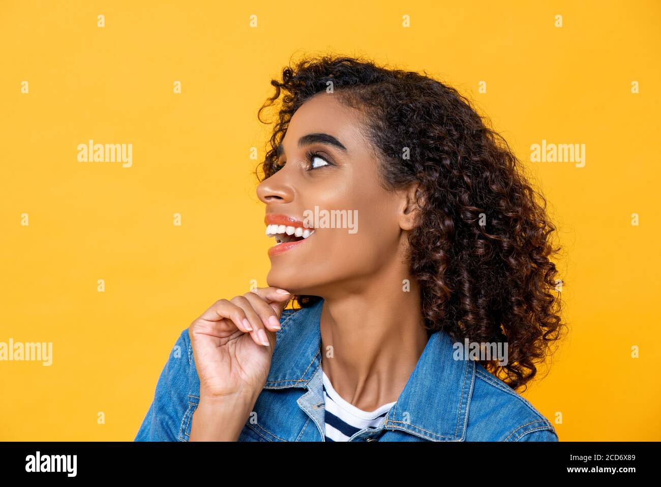 Nahaufnahme Porträt der jungen lächelnden afroamerikanischen Frau suchen An der Seite mit Hand berühren Kinn auf Studio gelb Studio Hintergrund Stockfoto