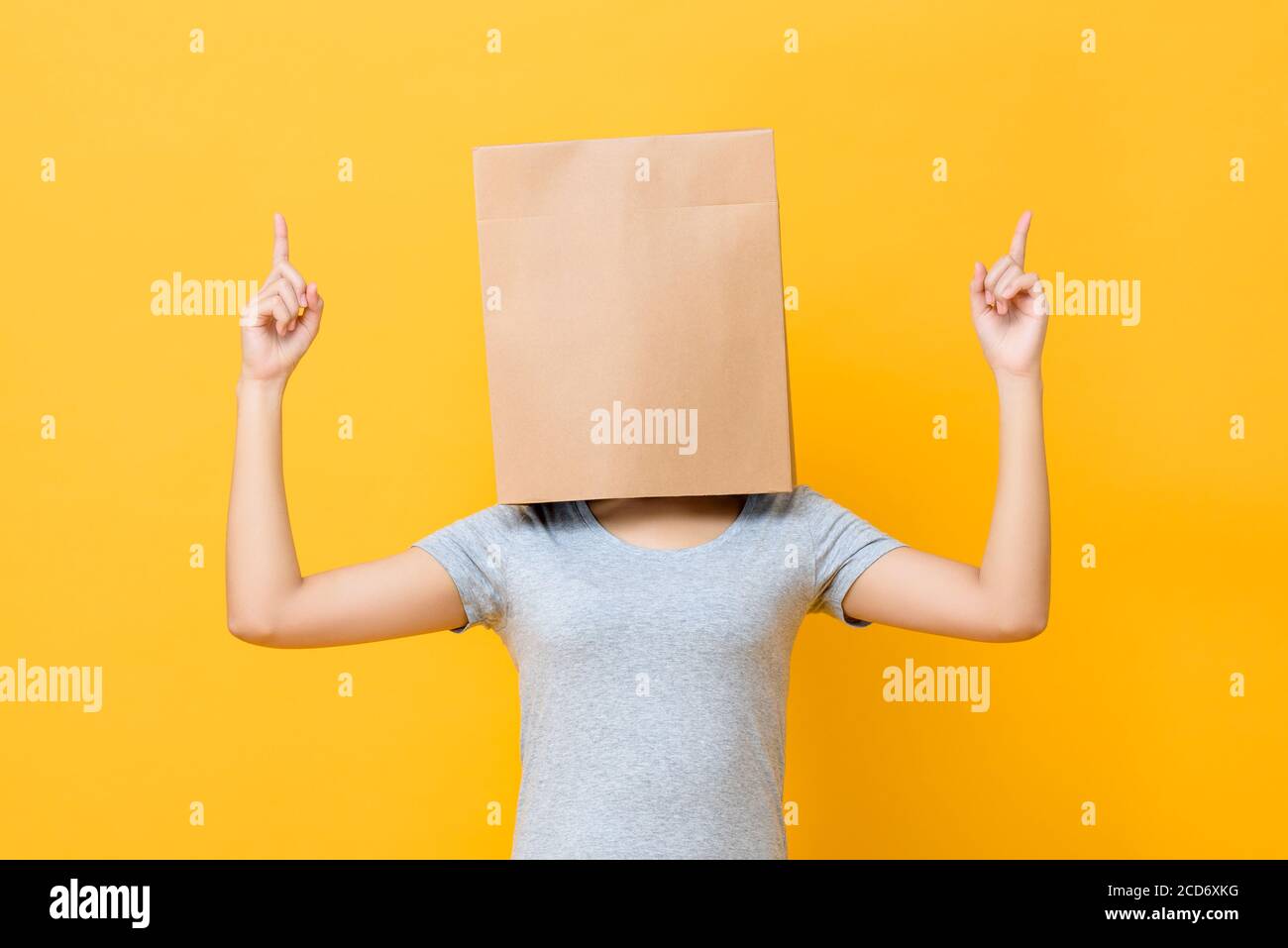 Konzept Porträt der anonymen Frau mit Kopf bedeckt mit Papier Tasche zeigt beide Finger nach oben in gelben Studio-Hintergrund Stockfoto